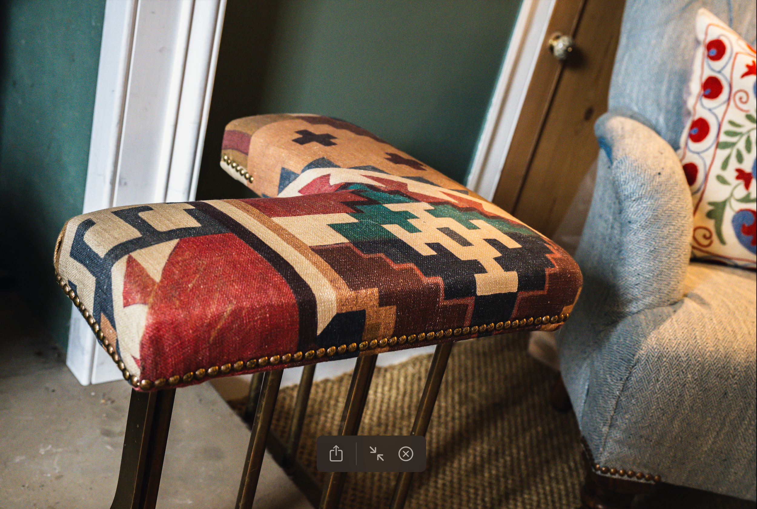 Three upholstered chairs with wooden legs, one with a southwestern pattern, one with a floral pattern, and another are arranged in a room with a green wall and wooden flooring.