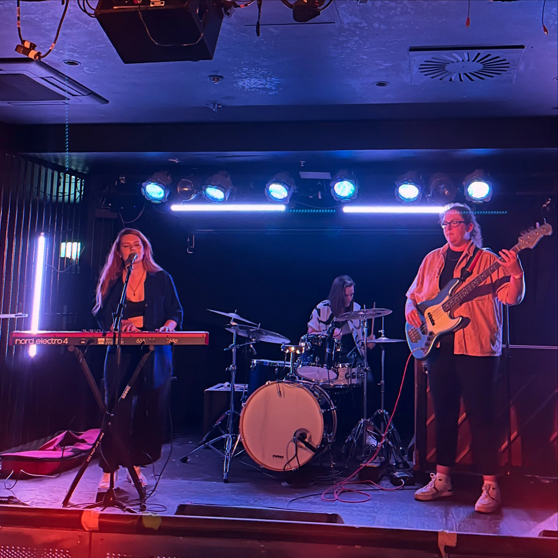 Miranda Joy and her band performing on stage with a keyboardist, drummer, and bassist under blue stage lights.