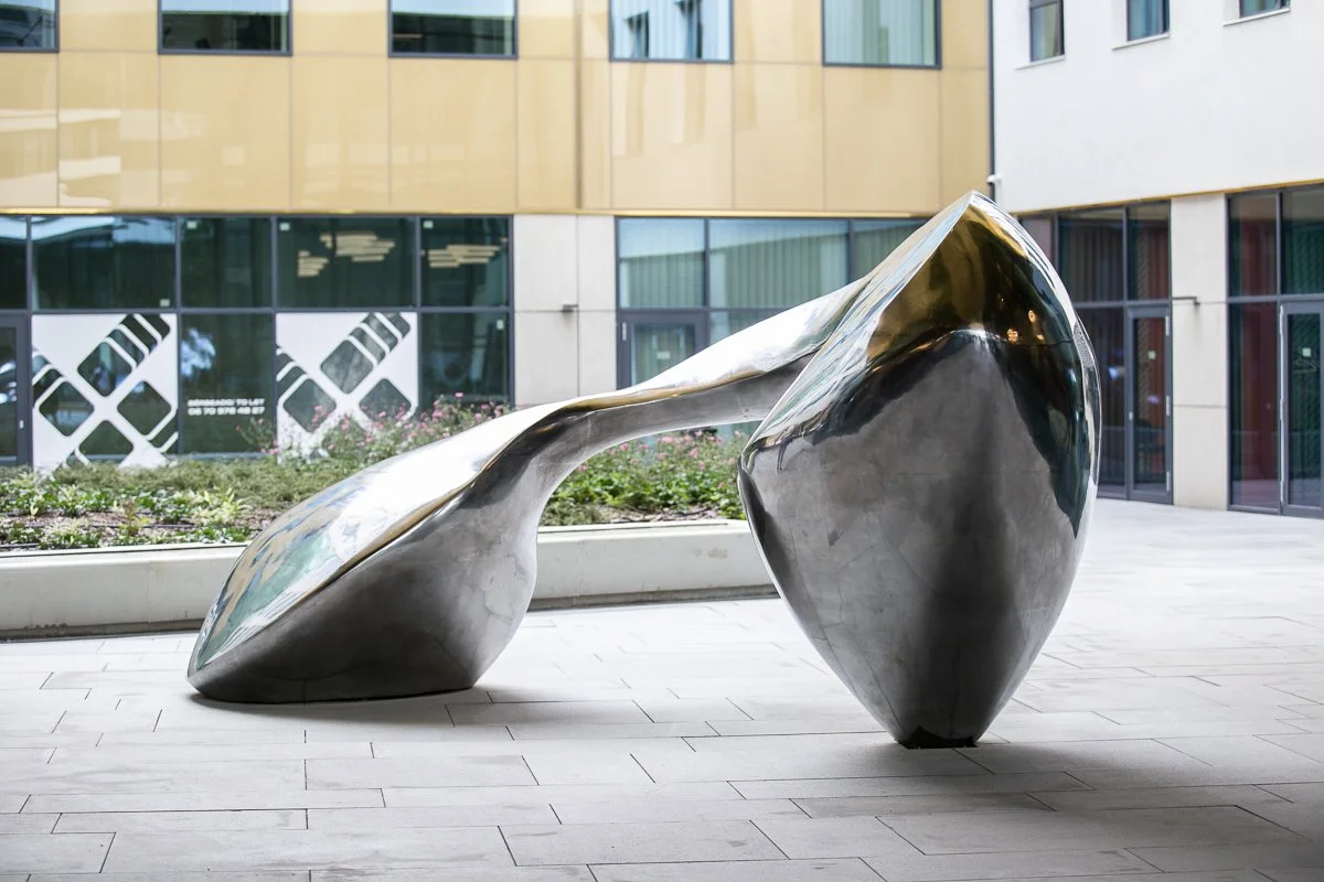 Modern abstract metal sculpture with rounded, flowing shapes in an outdoor urban setting.