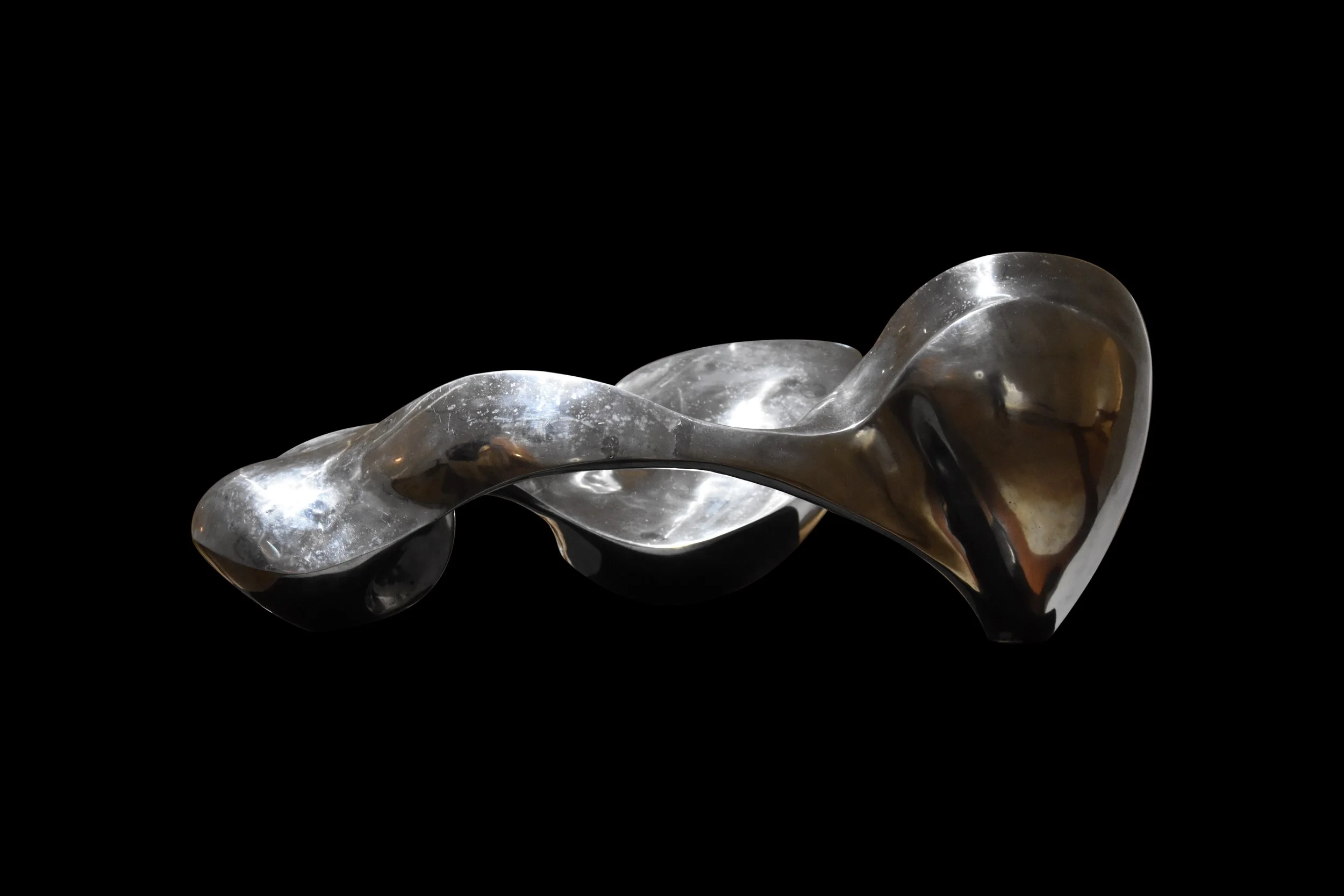 Abstract metallic sculpture with a flowing, twisted form against a black background.