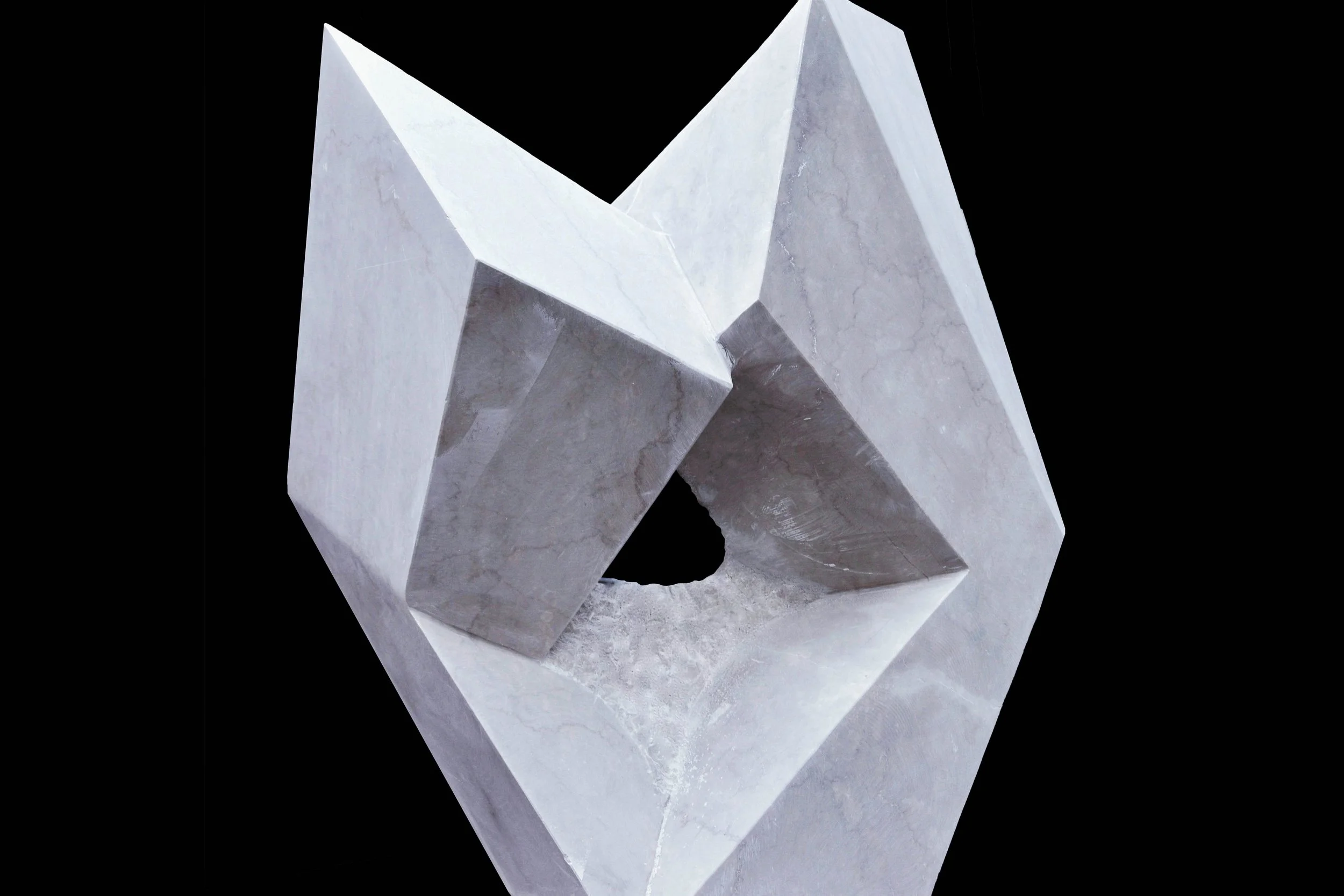 A modern sculpture made of concrete with geometric shapes and sharp angles, set against a black background.