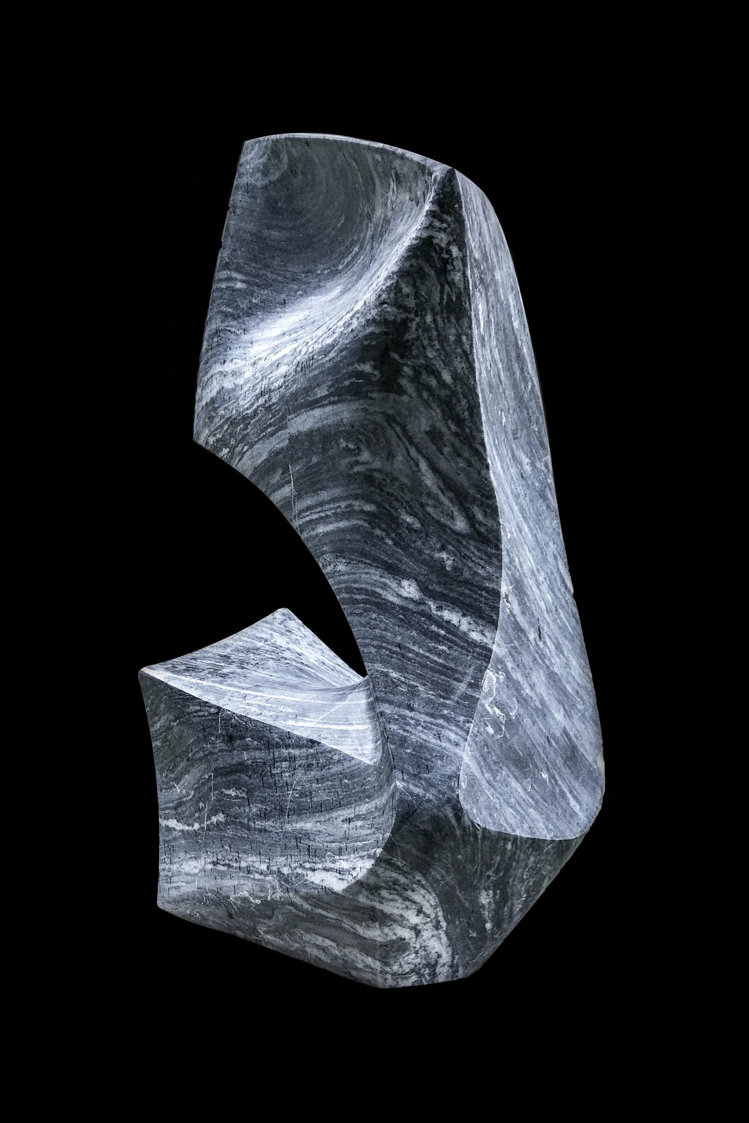 A black and white abstract sculpture with swirling patterns, mounted on a black background.