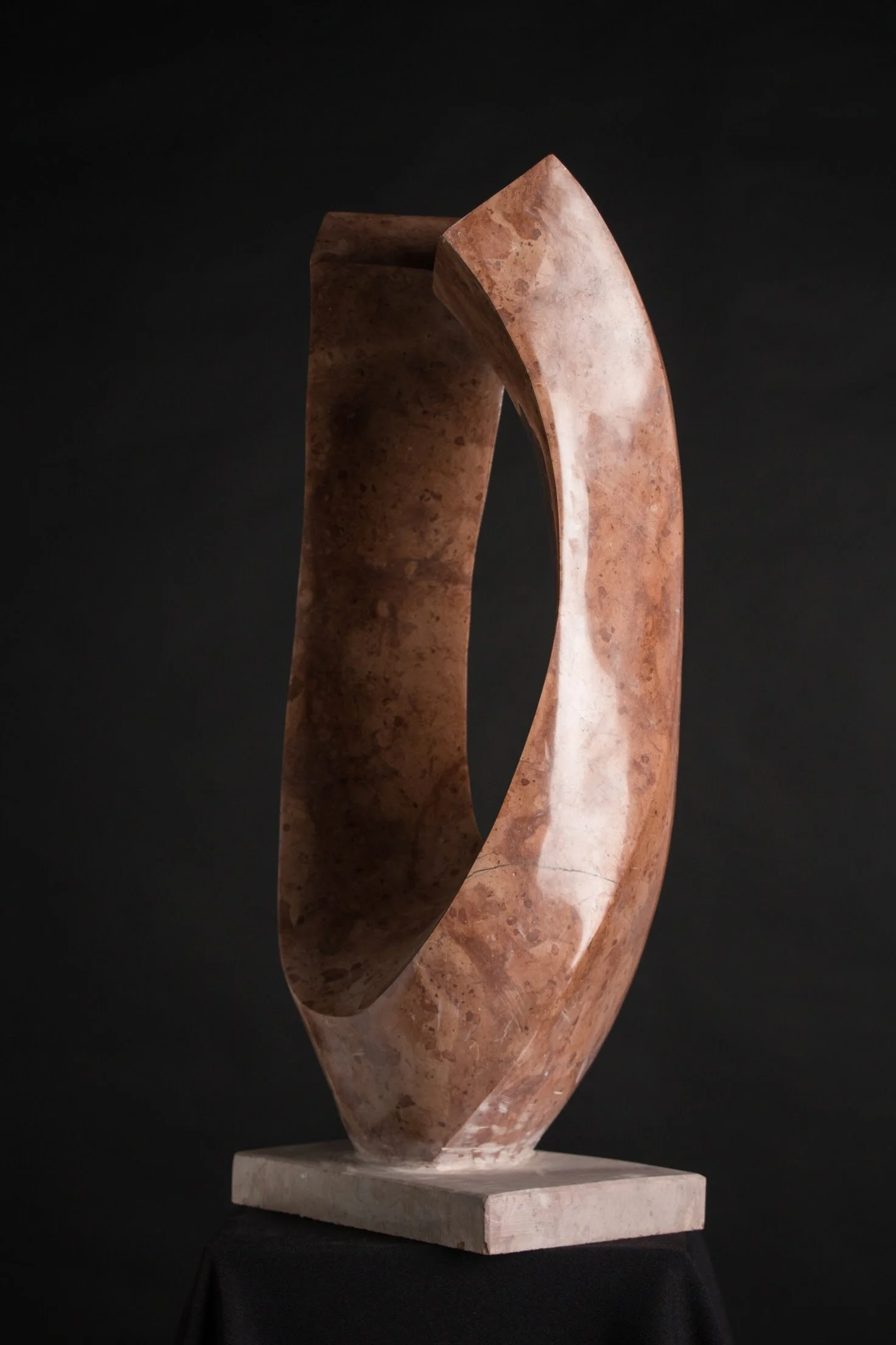 Abstract sculpture made of pink and brown marble, standing on a white marble base against a black background.