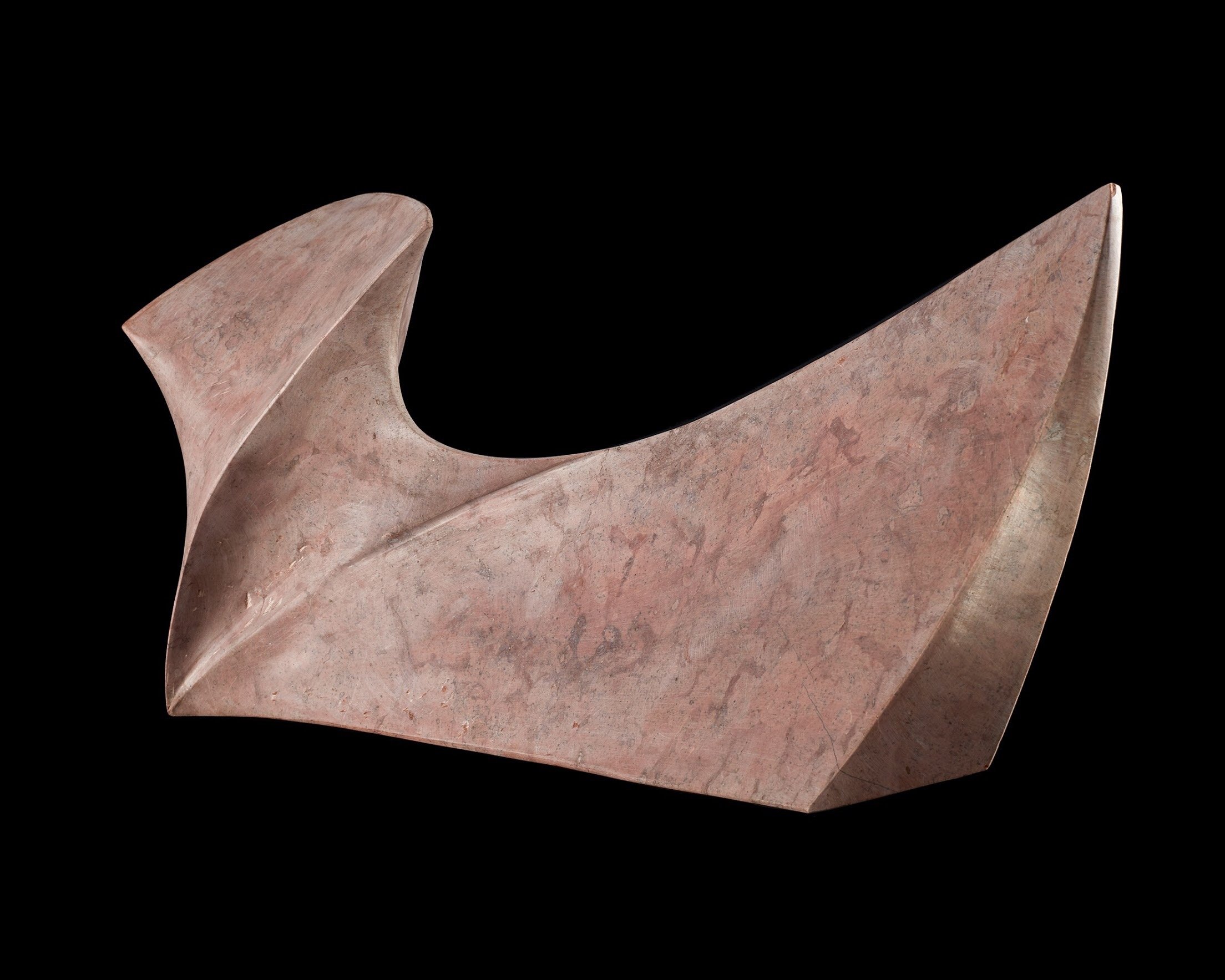A modern, abstract sculpture made of pinkish stone, featuring smooth, curving, and angular shapes set against a black background.