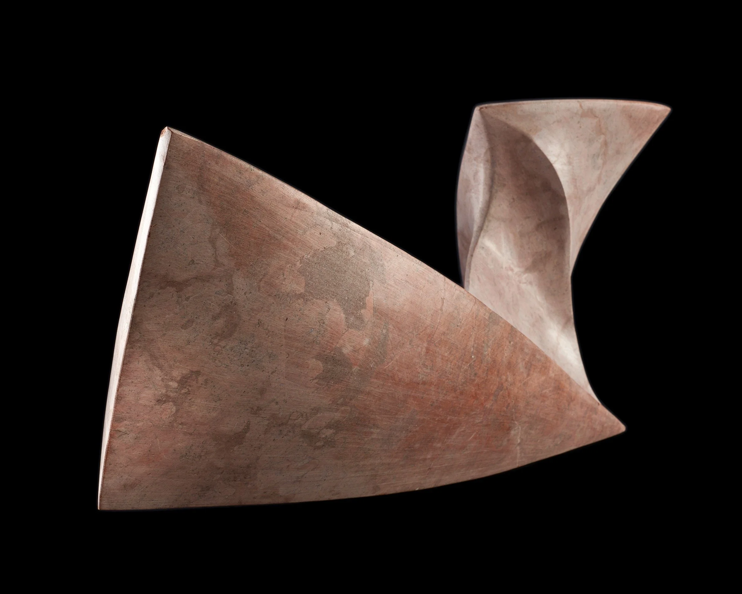 A metallic sculpture with geometric shapes, featuring a triangular base and a curved, folded element protruding upward, set against a black background.