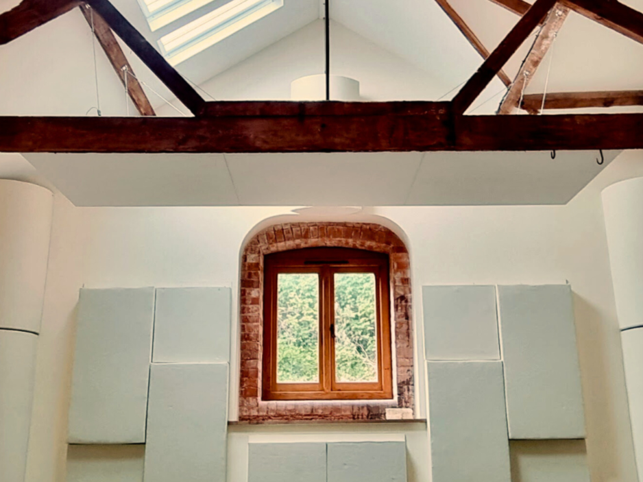Interior view of a room with a wooden ceiling beam, brick-framed window, skylight, and soundproofed walls.
