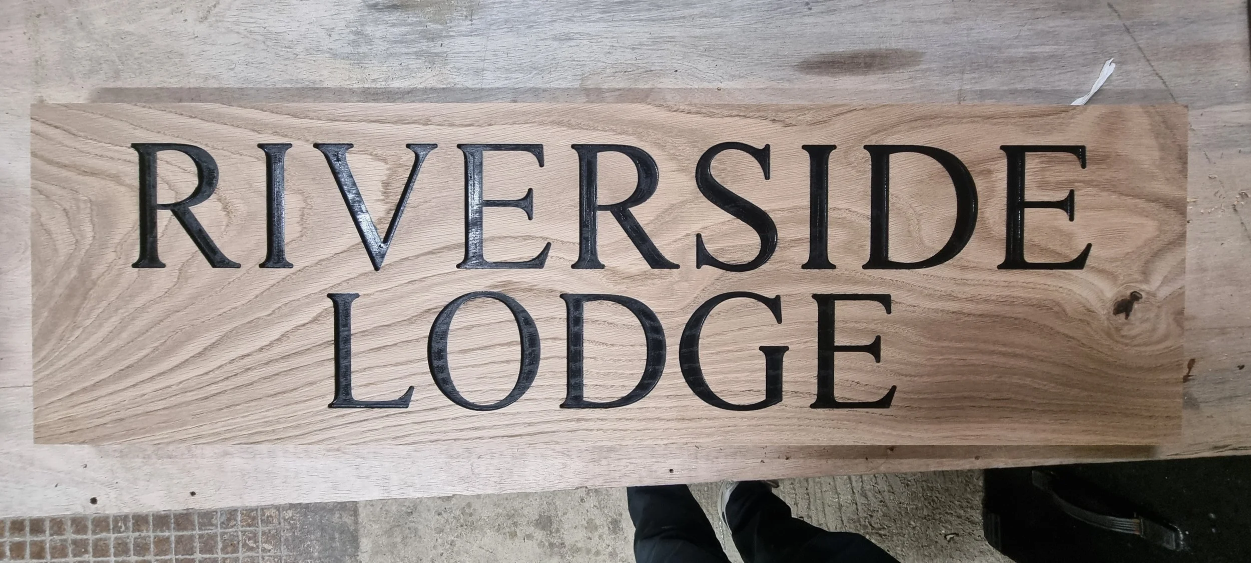 A wooden sign with the text "RIVERSIDE LODGE" carved and painted in black.