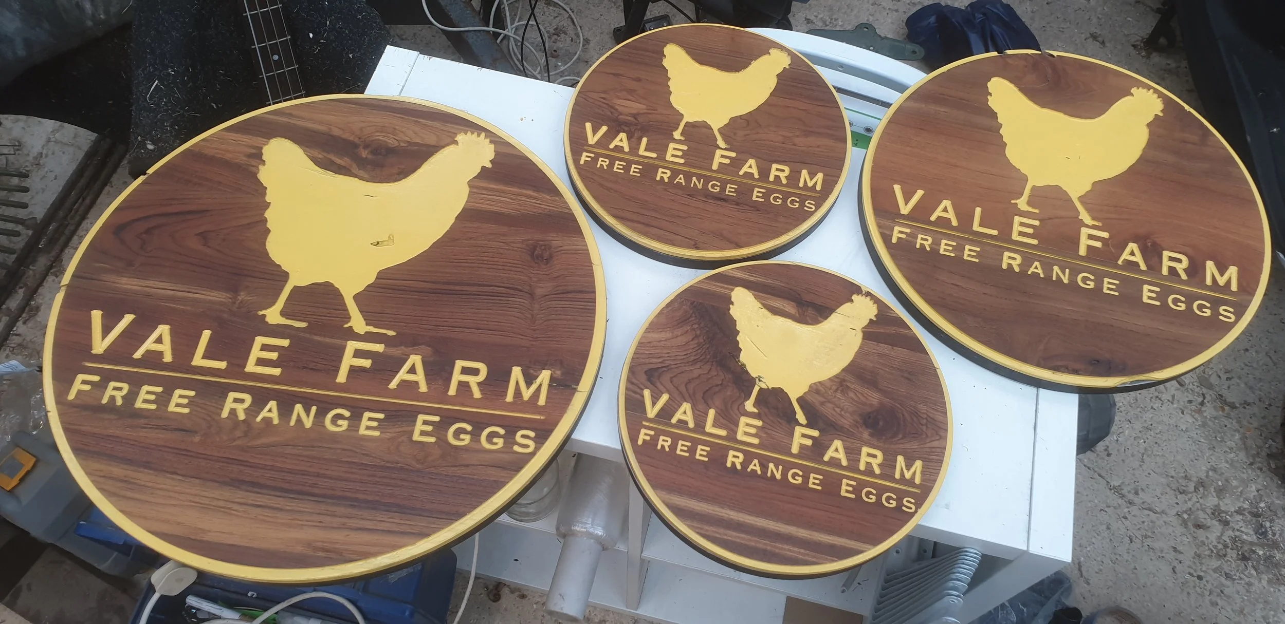 Four wooden round signs with a yellow chicken silhouette and yellow text that reads "Vale Farm Free Range Eggs."