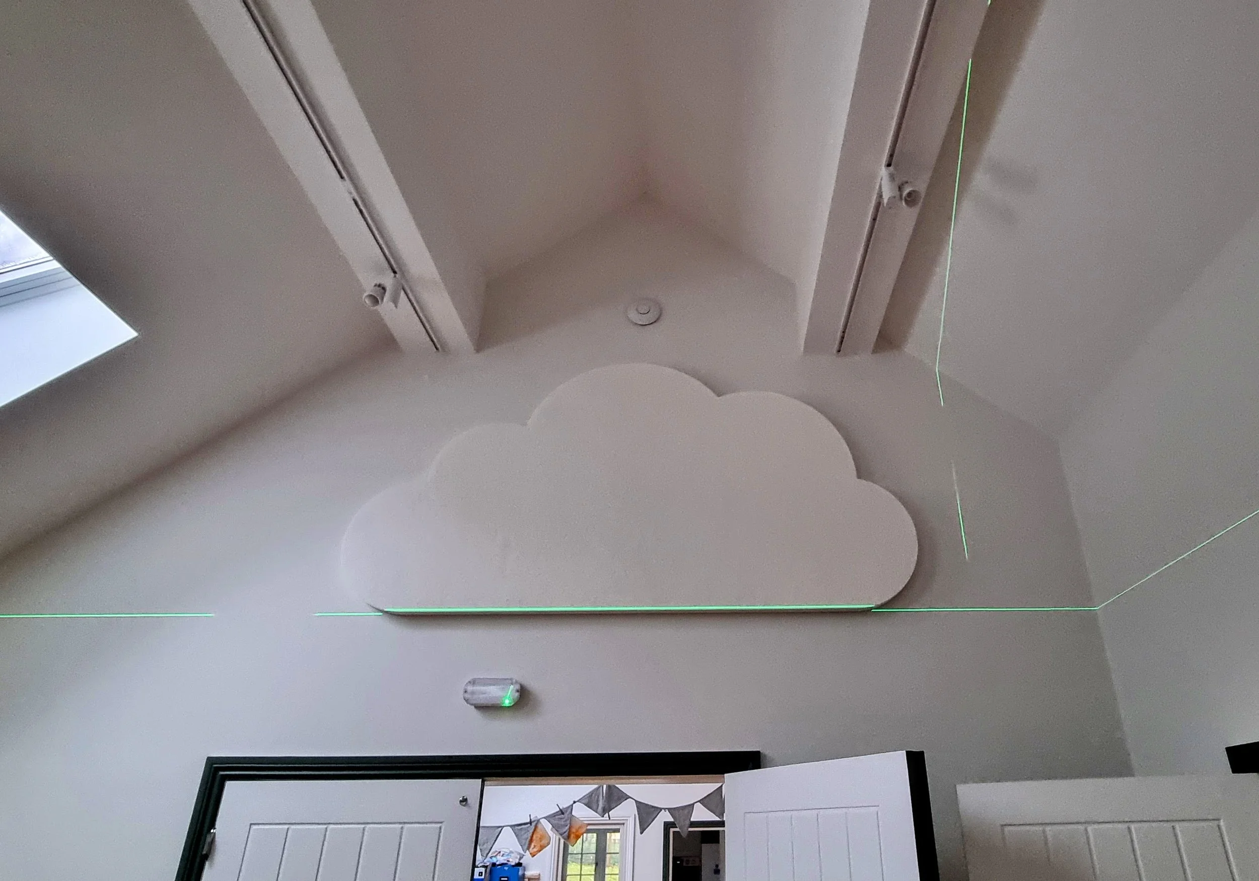 Cloud-shaped white wall decoration on a ceiling, with green laser lines projecting across the room.