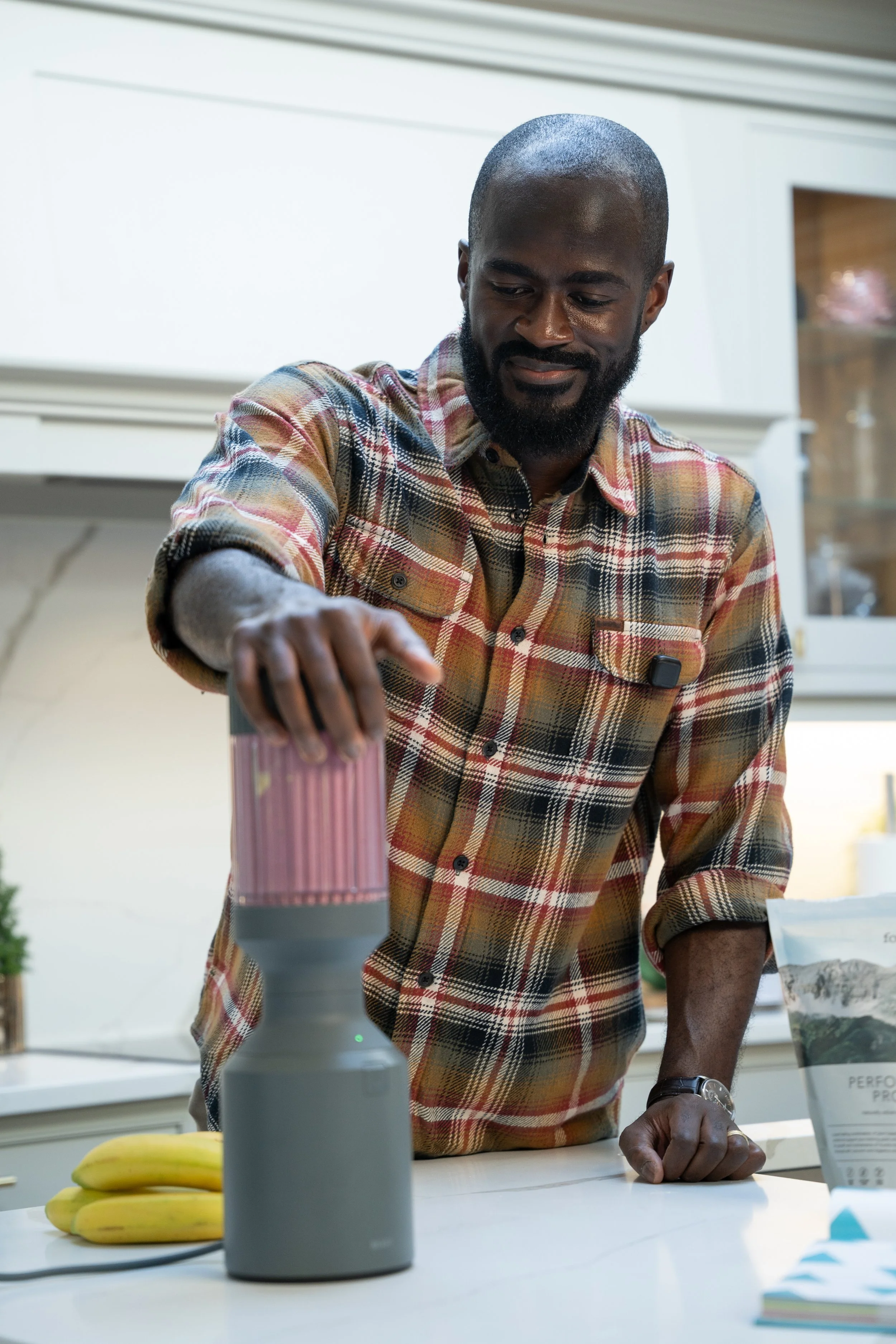A man blending a smoothie in a kitchen with bananas on the table.
