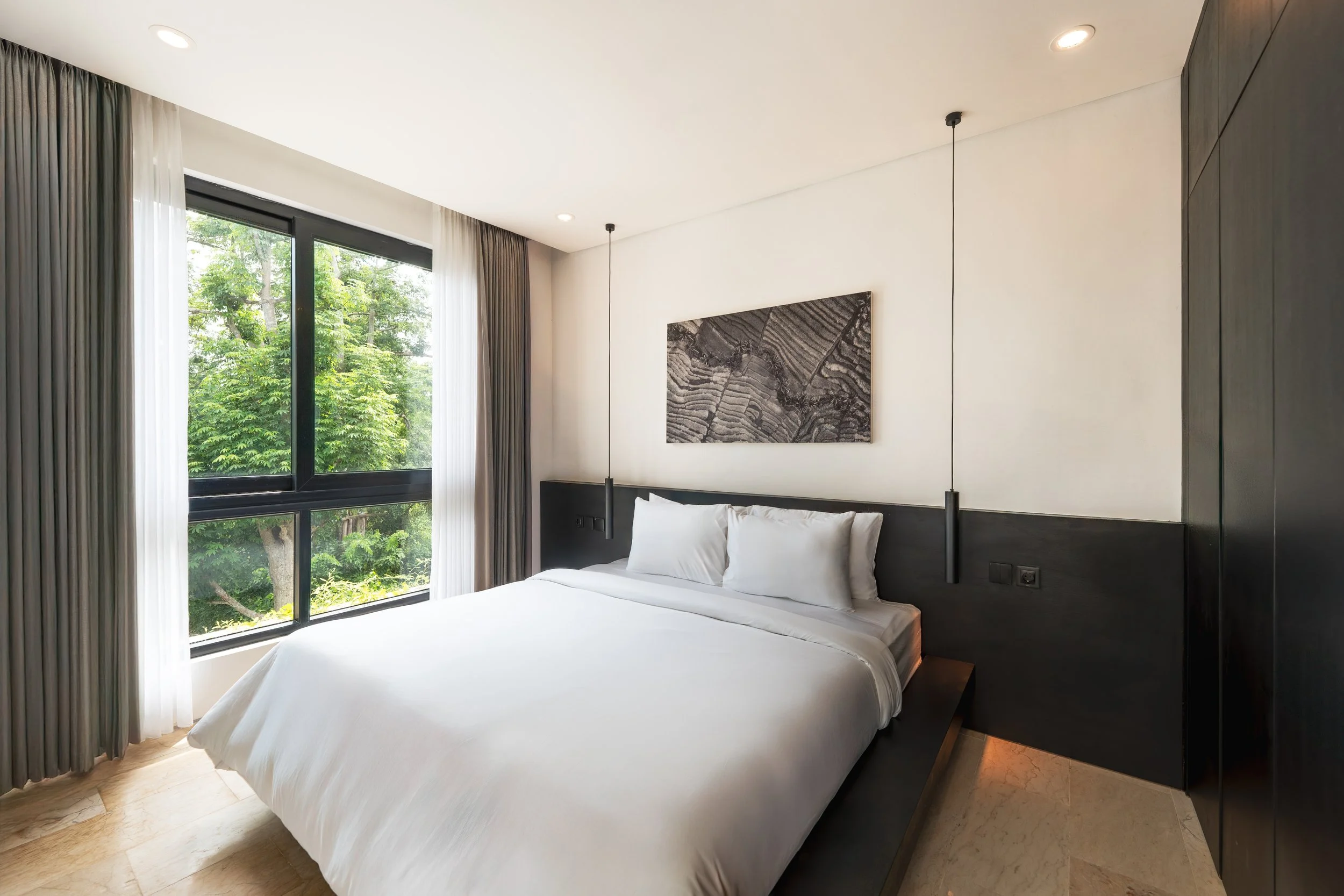 Modern bedroom with large window, white bedding, dark headboard, black pendant lights, and minimalistic decor.