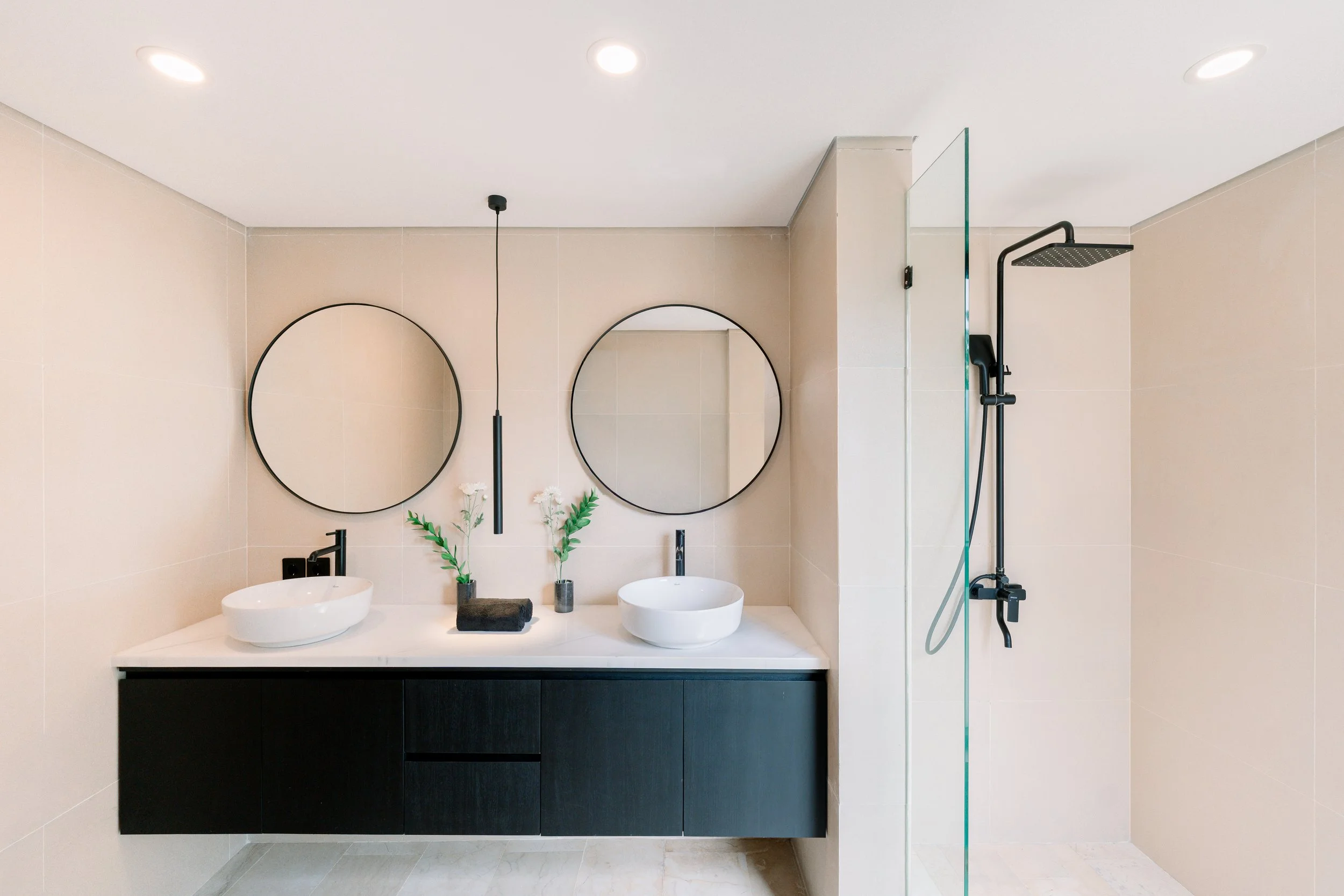 Modern bathroom with double vanity featuring two round mirrors, sleek black fixtures, and a walk-in shower with black hardware and a glass partition.