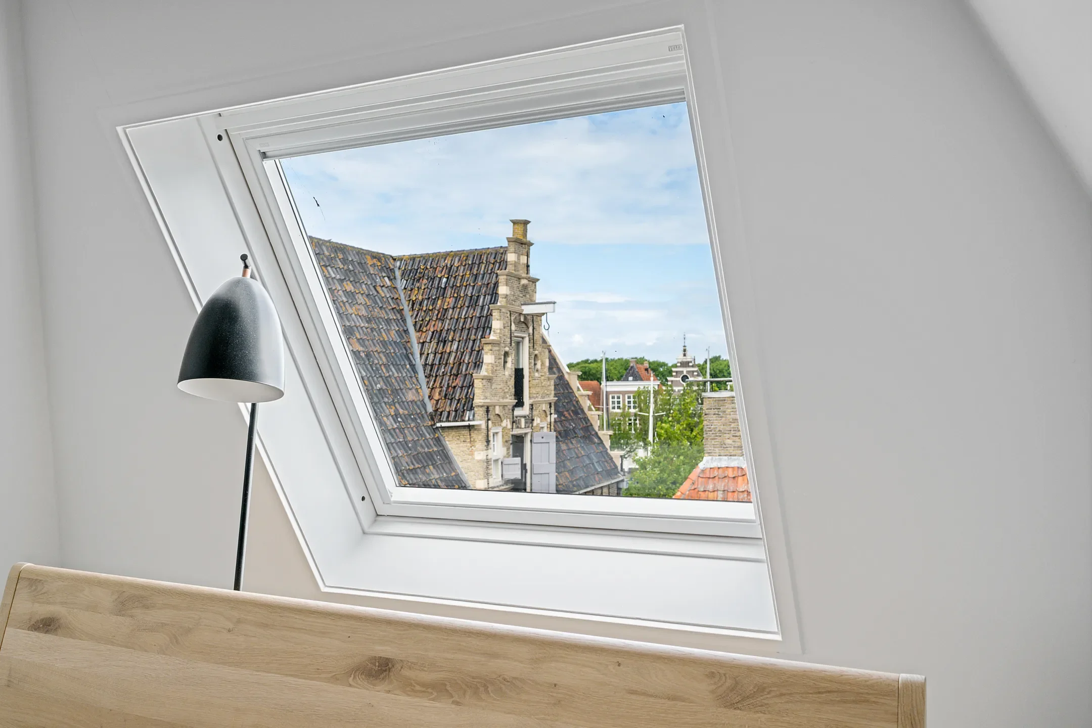 View through a skylight window showing rooftops and buildings outside on a partly cloudy day.