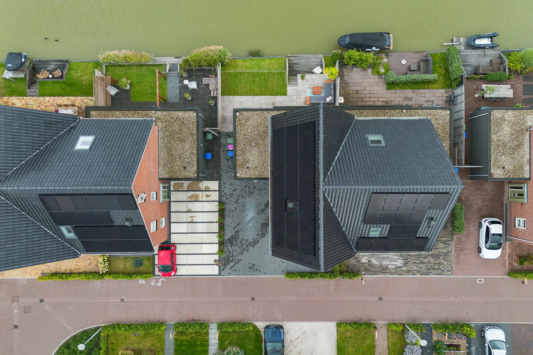 Aerial view of residential houses along a canal, with driveways, cars, and small yards.
