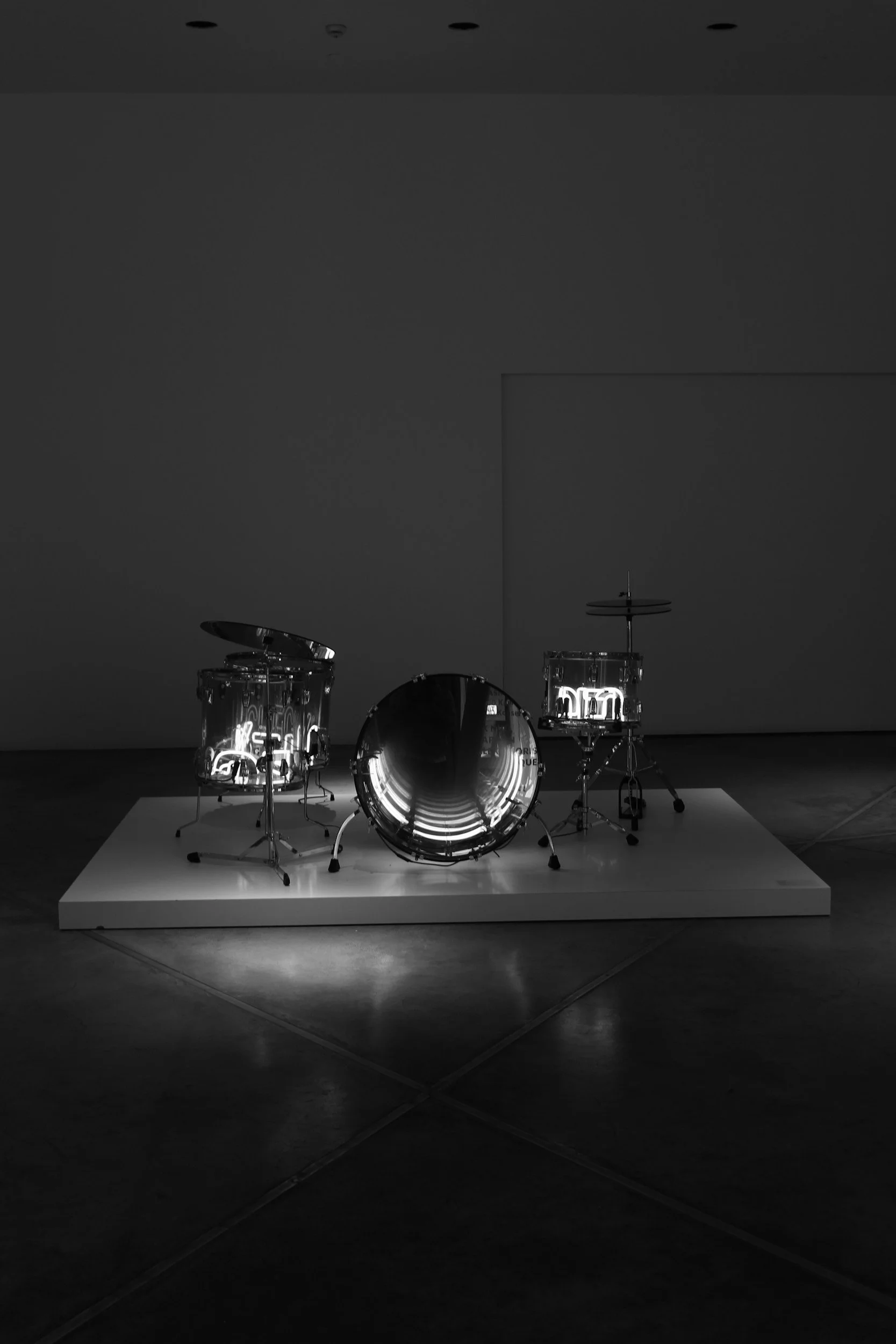 A drum set illuminated by neon lights on a white platform in a dark room