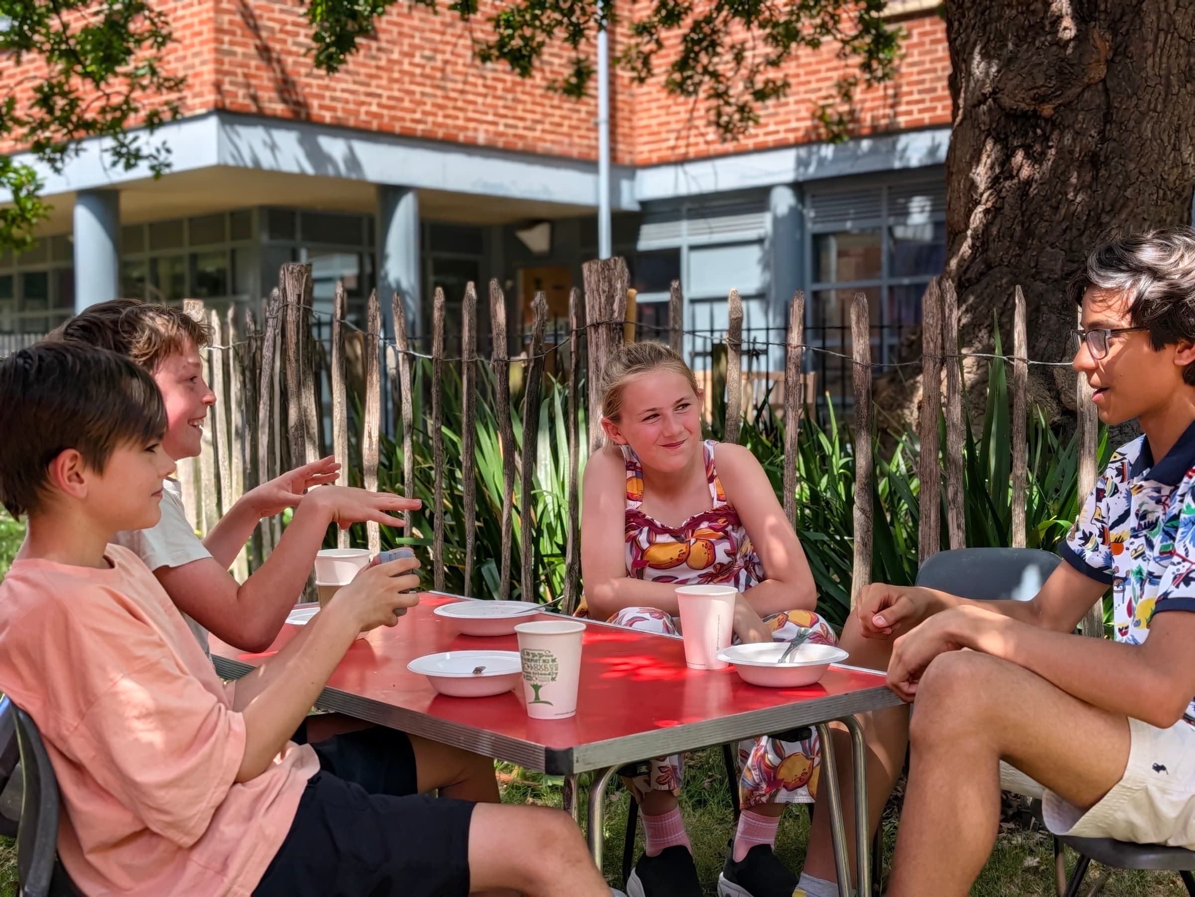 Smiling children sit around a table in the church garden talking