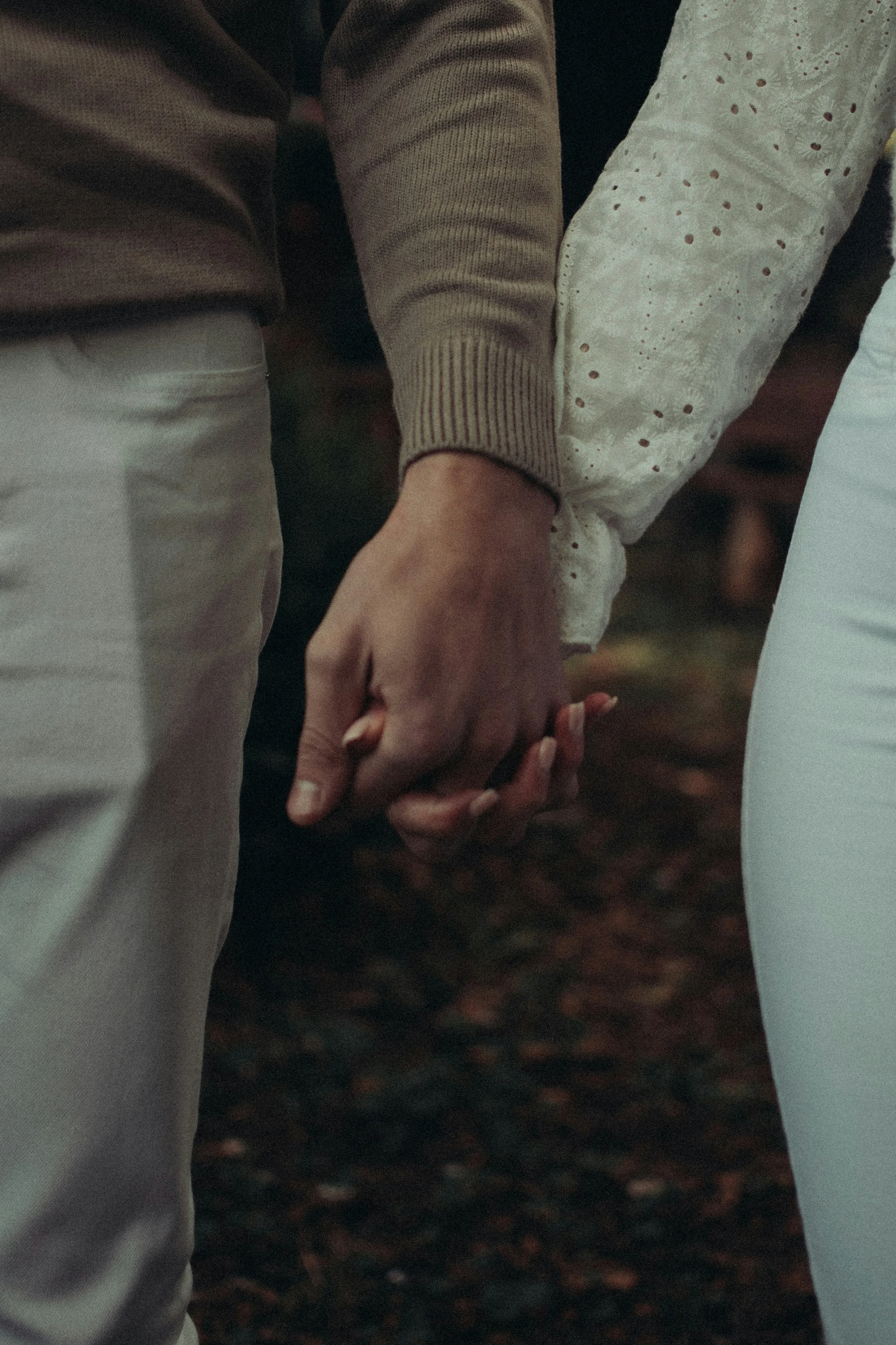 Two people holding hands, one wearing a beige sweater and the other wearing a white speckled sweater, standing close together.