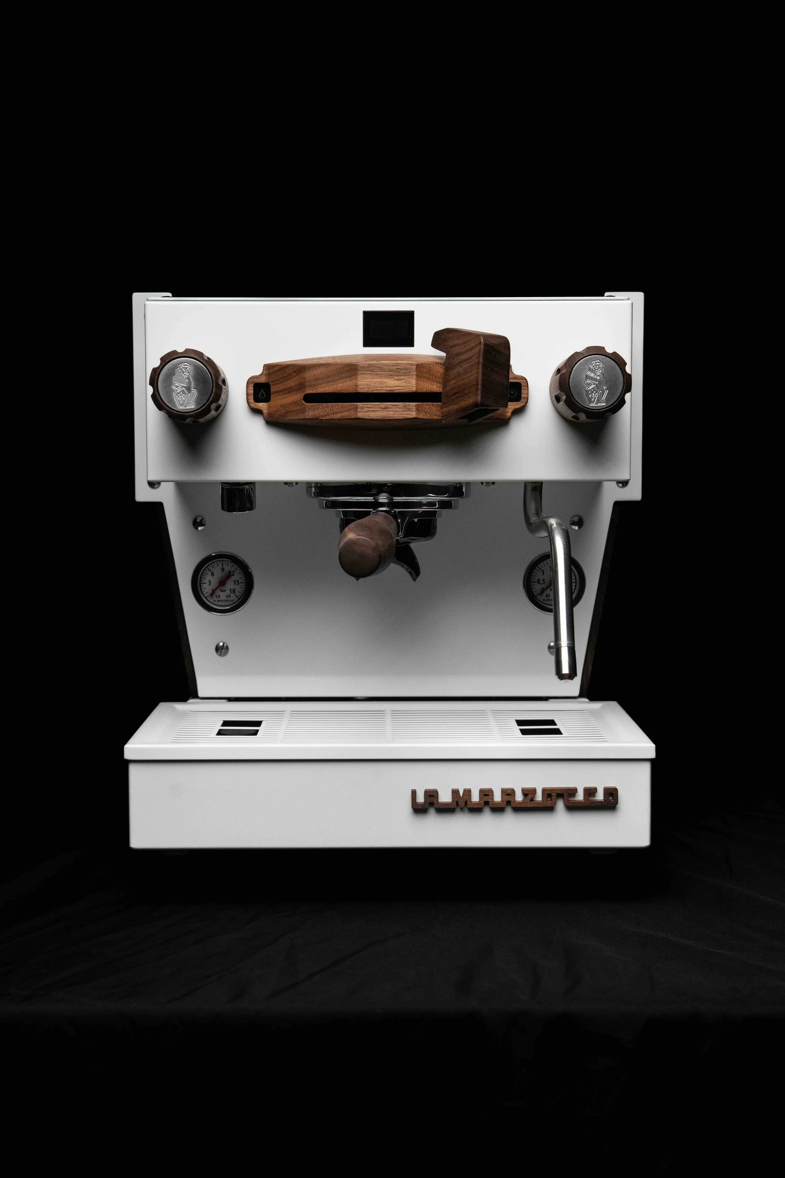 A white La Marzocco espresso machine with wooden accents and black knobs, set against a black background.
