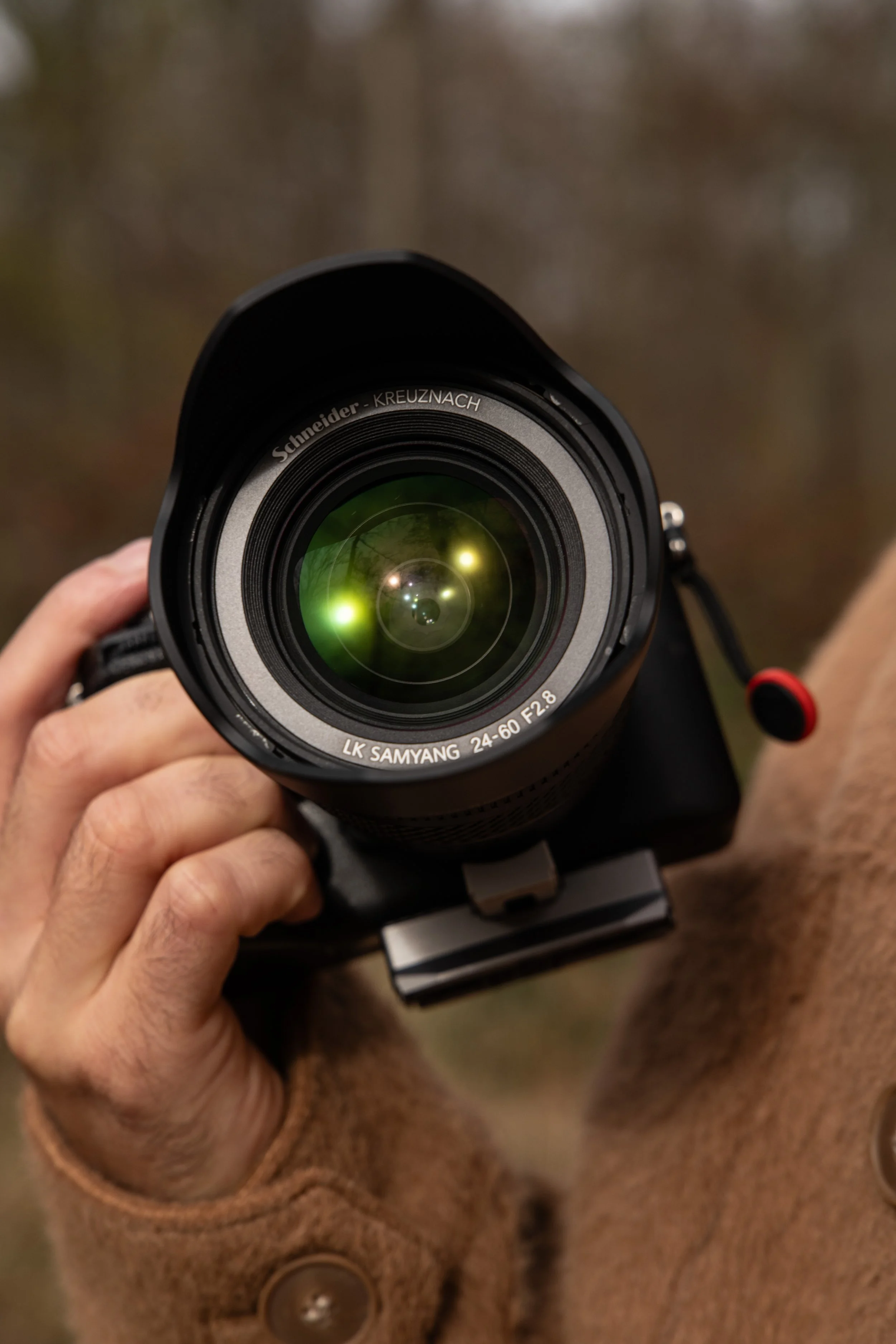 Close-up of a person holding a professional camera lens, with a blurred outdoor background.