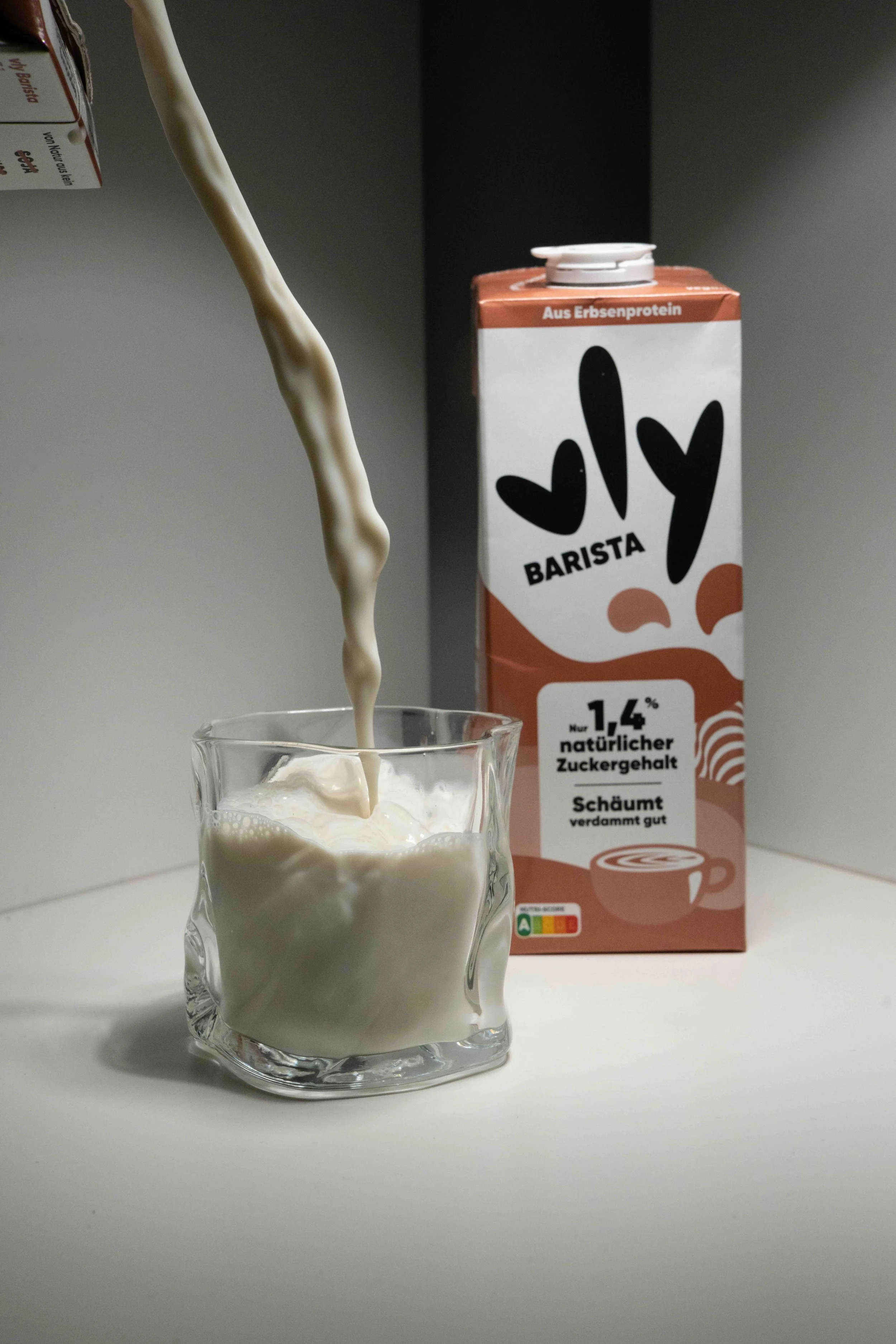 Pouring plant-based milk into a glass with a carton of plant-based milk in the background.
