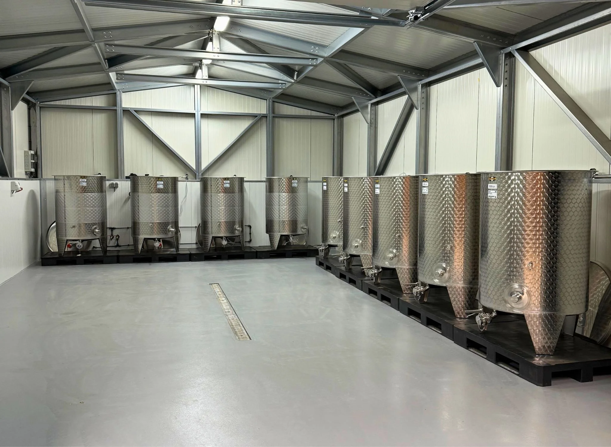 Binnenruimte met negen grote roestvrijstalen vaten op zwarte pallets,  voor opslag van onze lokale wijn uit Zeeuws Vlaanderen.