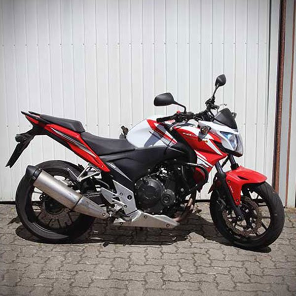 Ein rotes und schwarzes Motorrad steht auf einer gepflasterten Oberfläche vor einer weißen Metallwand.