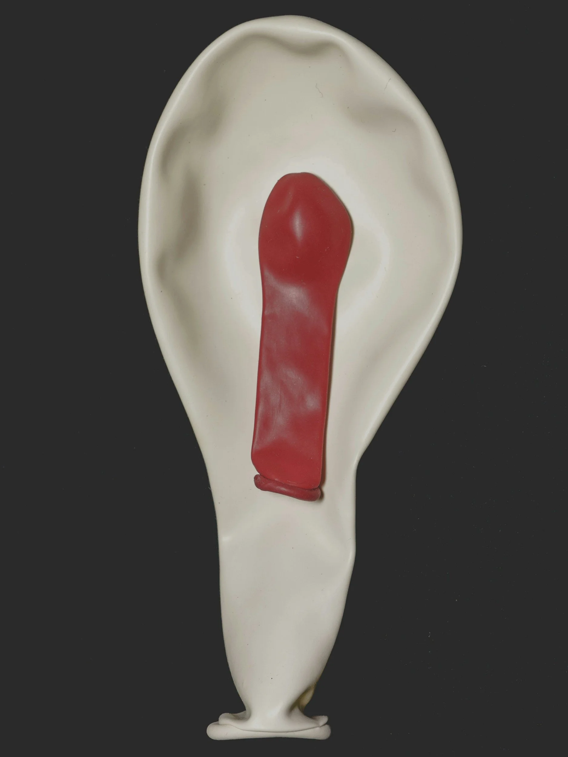 A white ceramic spoon with a red handle and tip, against a black background.