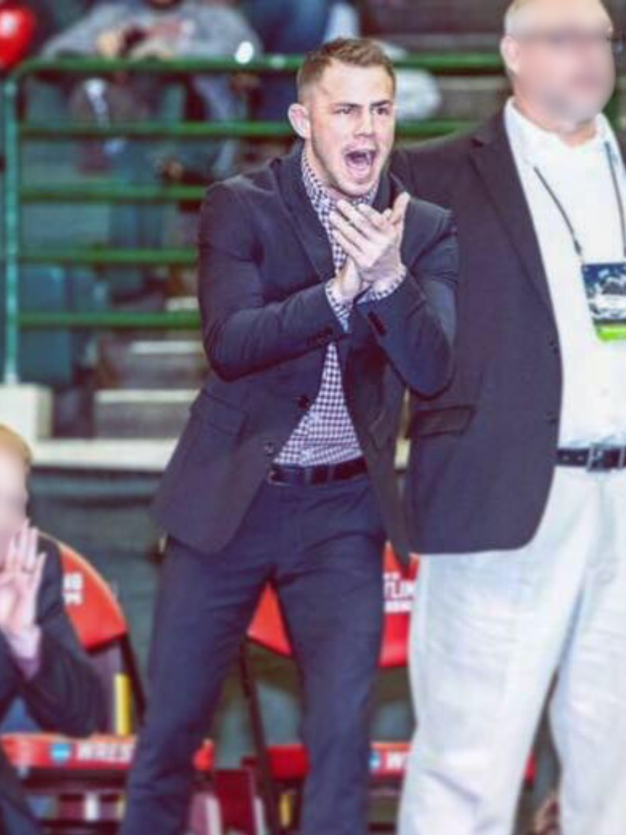 Portrait of a man with short brown hair, beard, smiling, wearing a dark suit, white shirt, and a light-colored tie against a plain background.