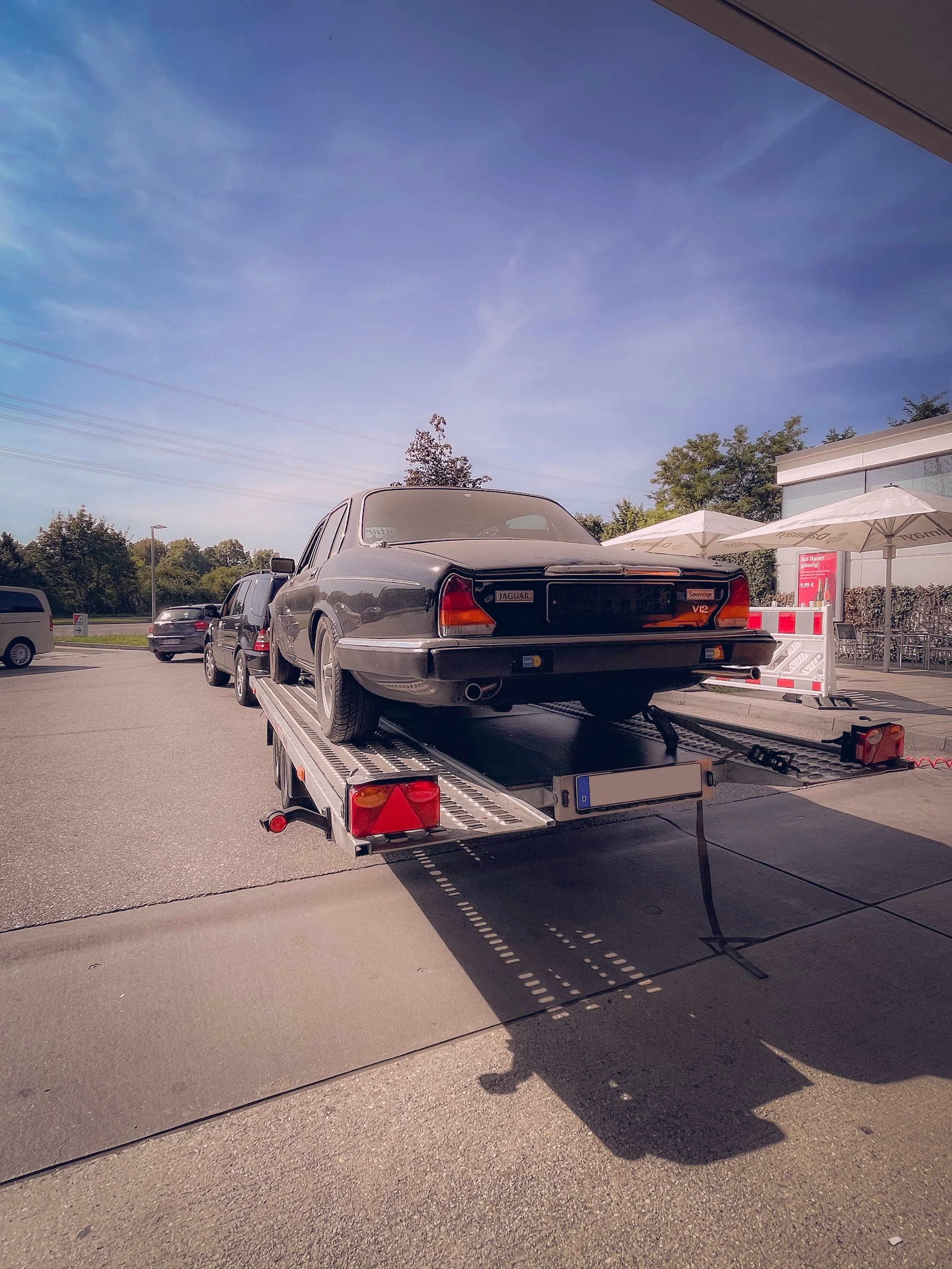 A black vintage Jaguar car on a flatbed tow truck in a parking lot.