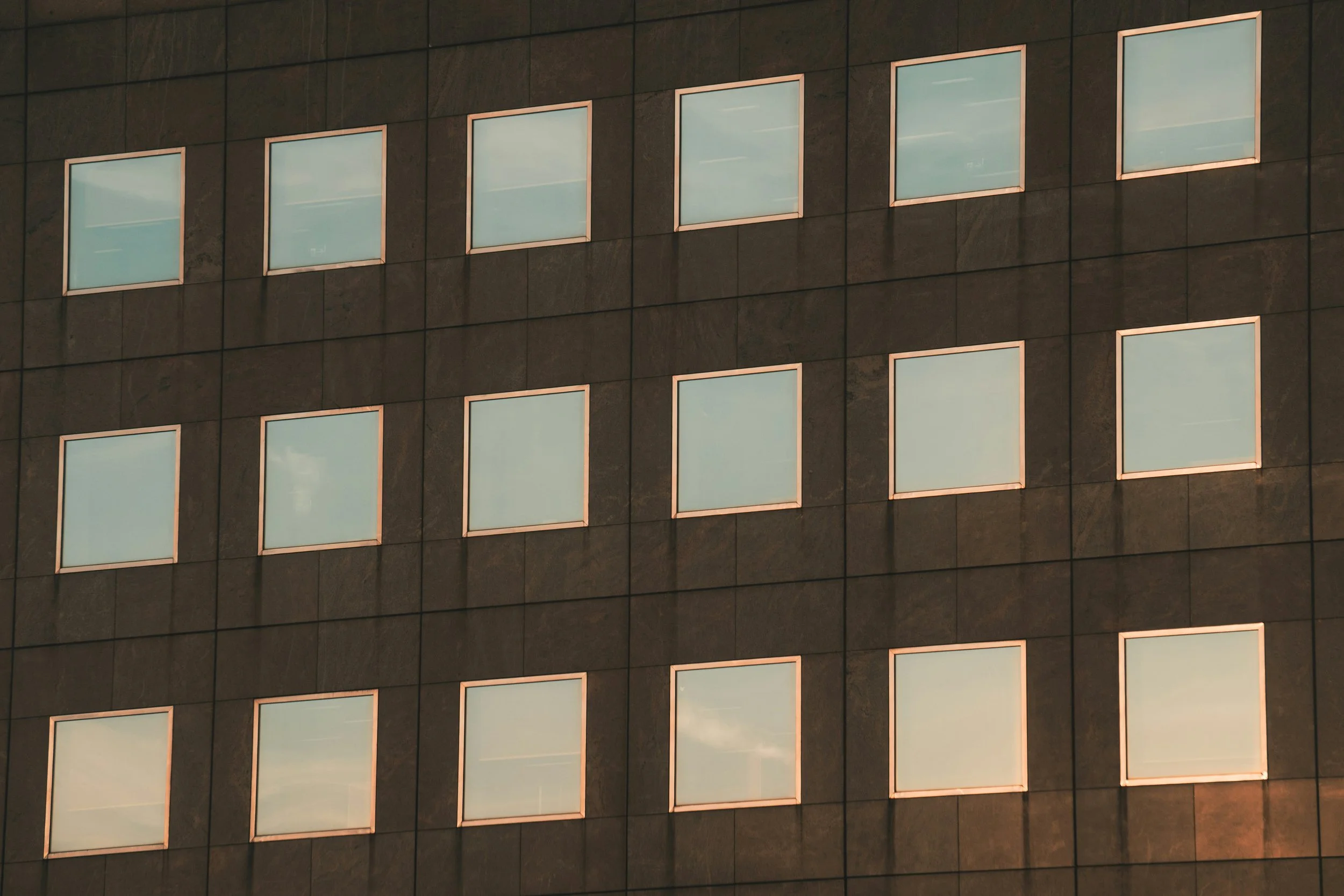 Corner of a modern building with multiple square windows reflecting the sky.
