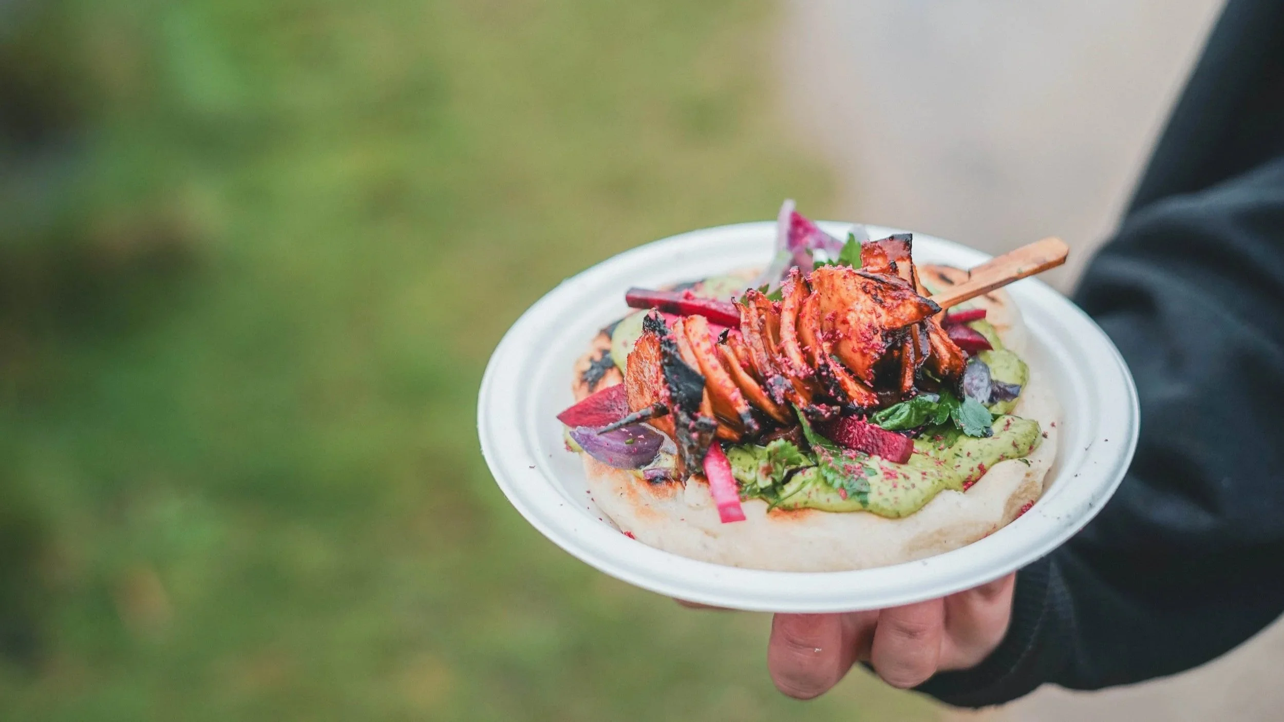 Person holding a white plate with vegan bbq skewers, dip, and vegetables on top.