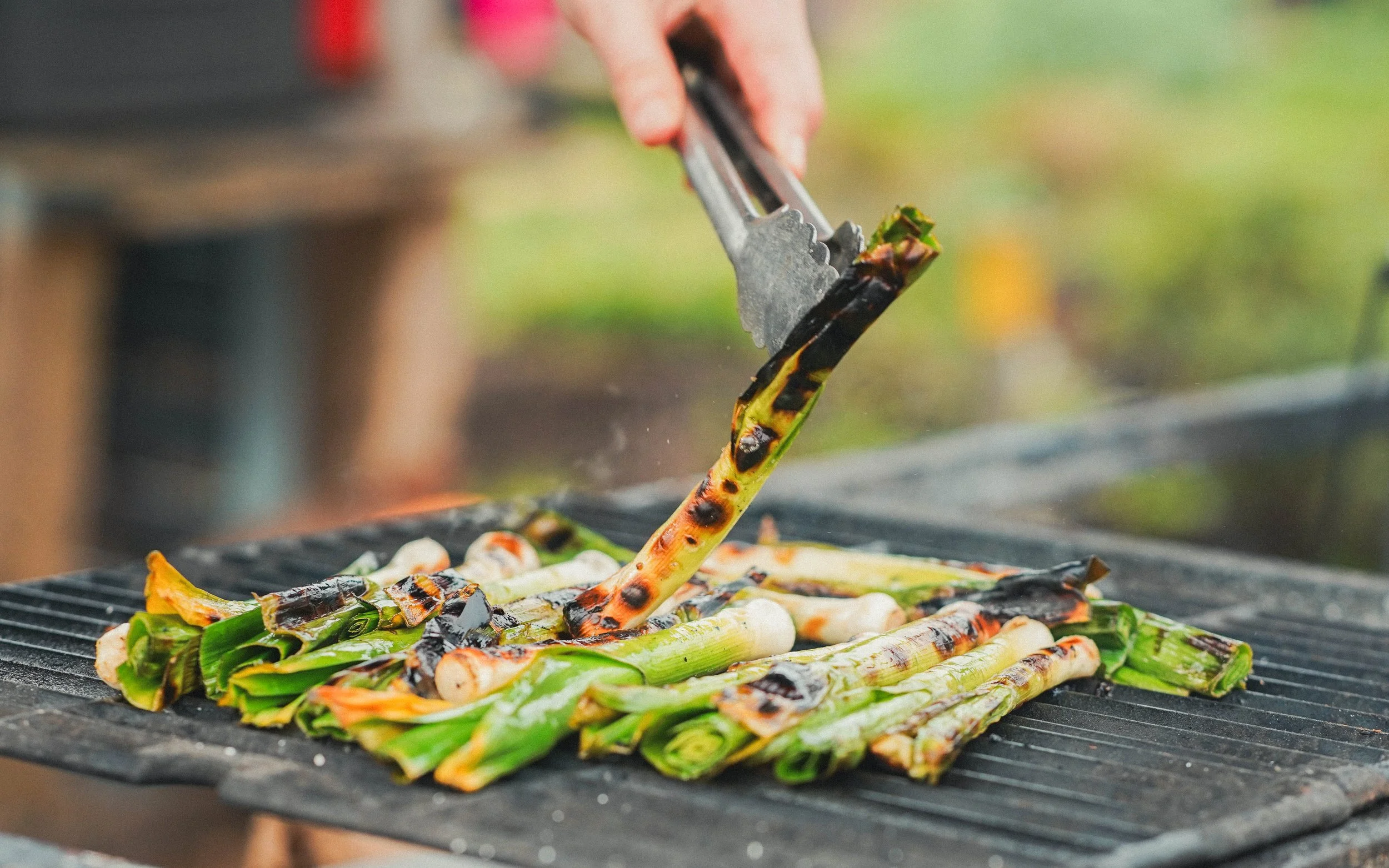 Person using tongs to grill asparagus spears with charred grill marks.