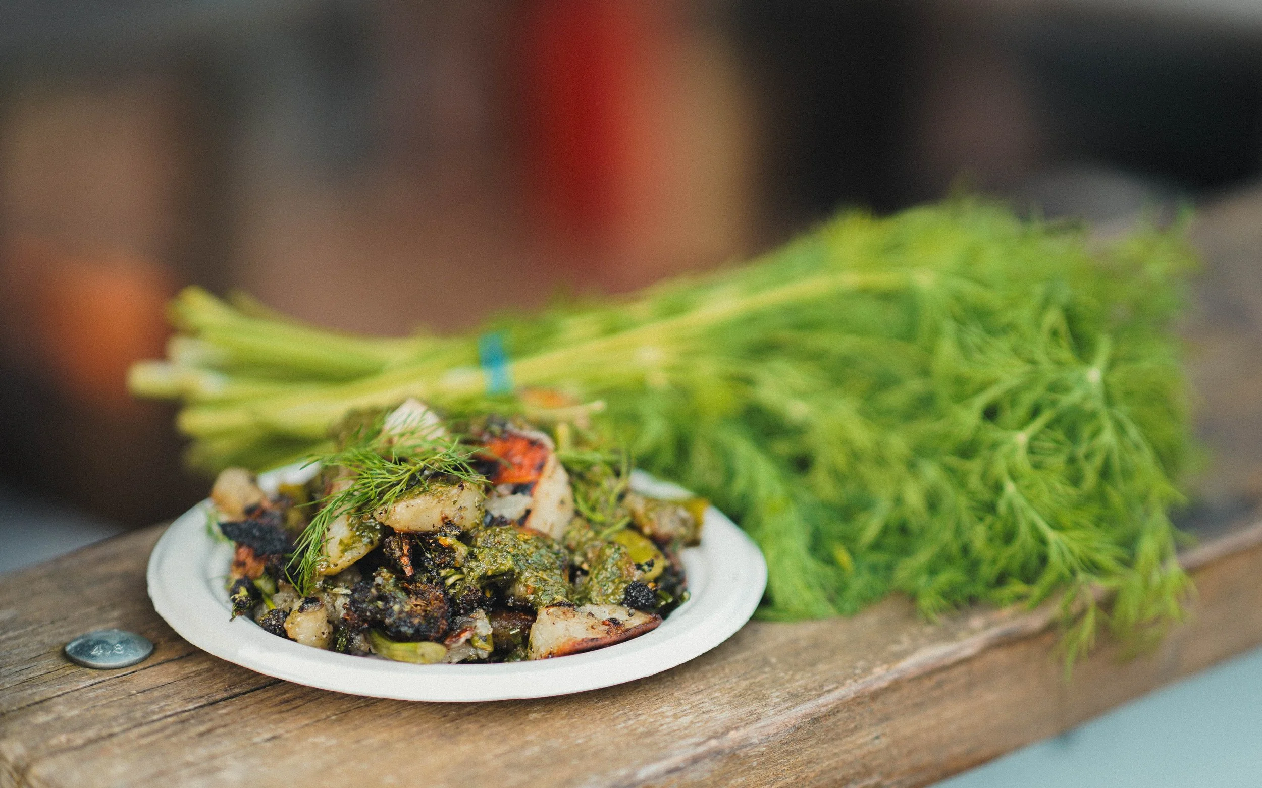Fresh dill and a plate of grilled vegetables on a wooden surface.