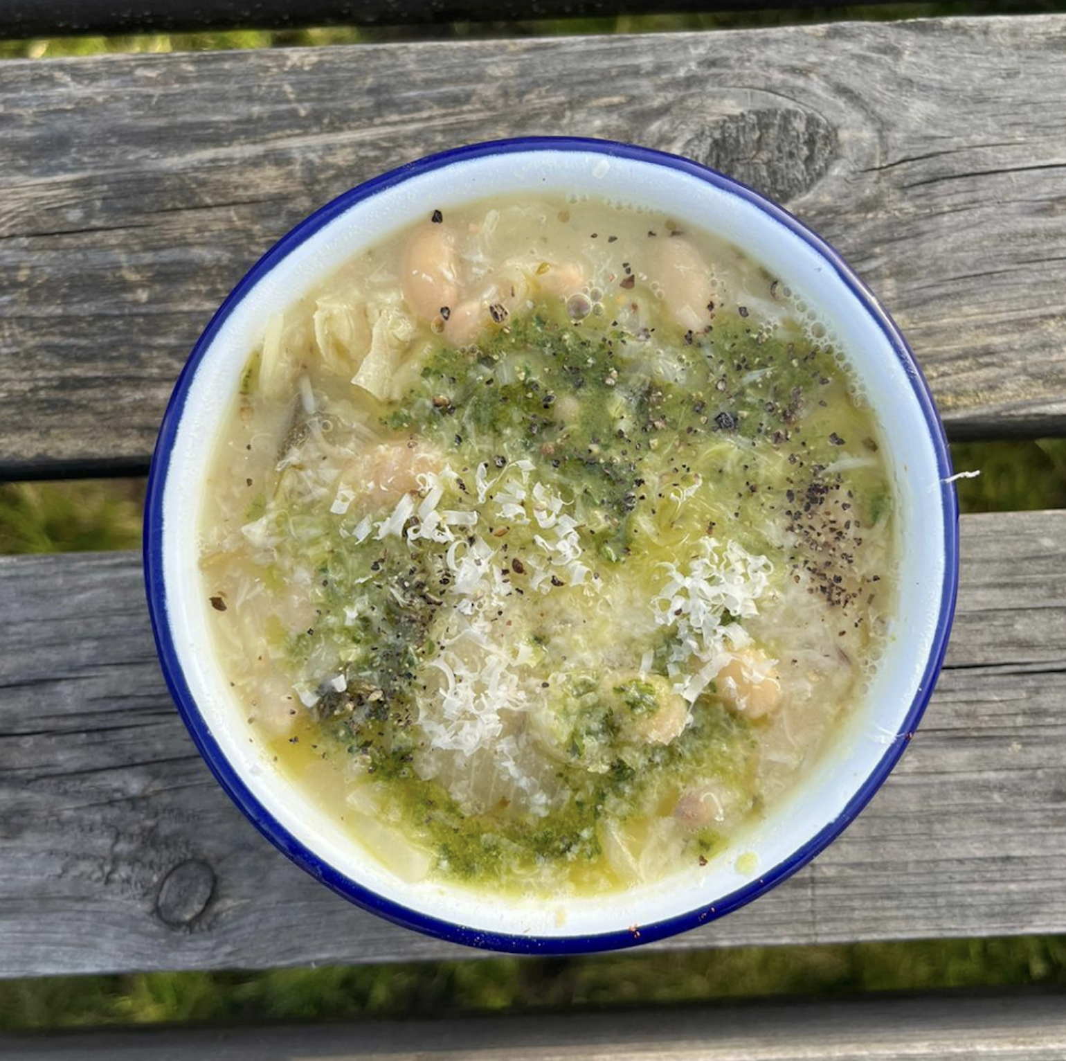 A bowl of homemade chicken soup with herbs and vegetables, placed on a wooden surface outside.