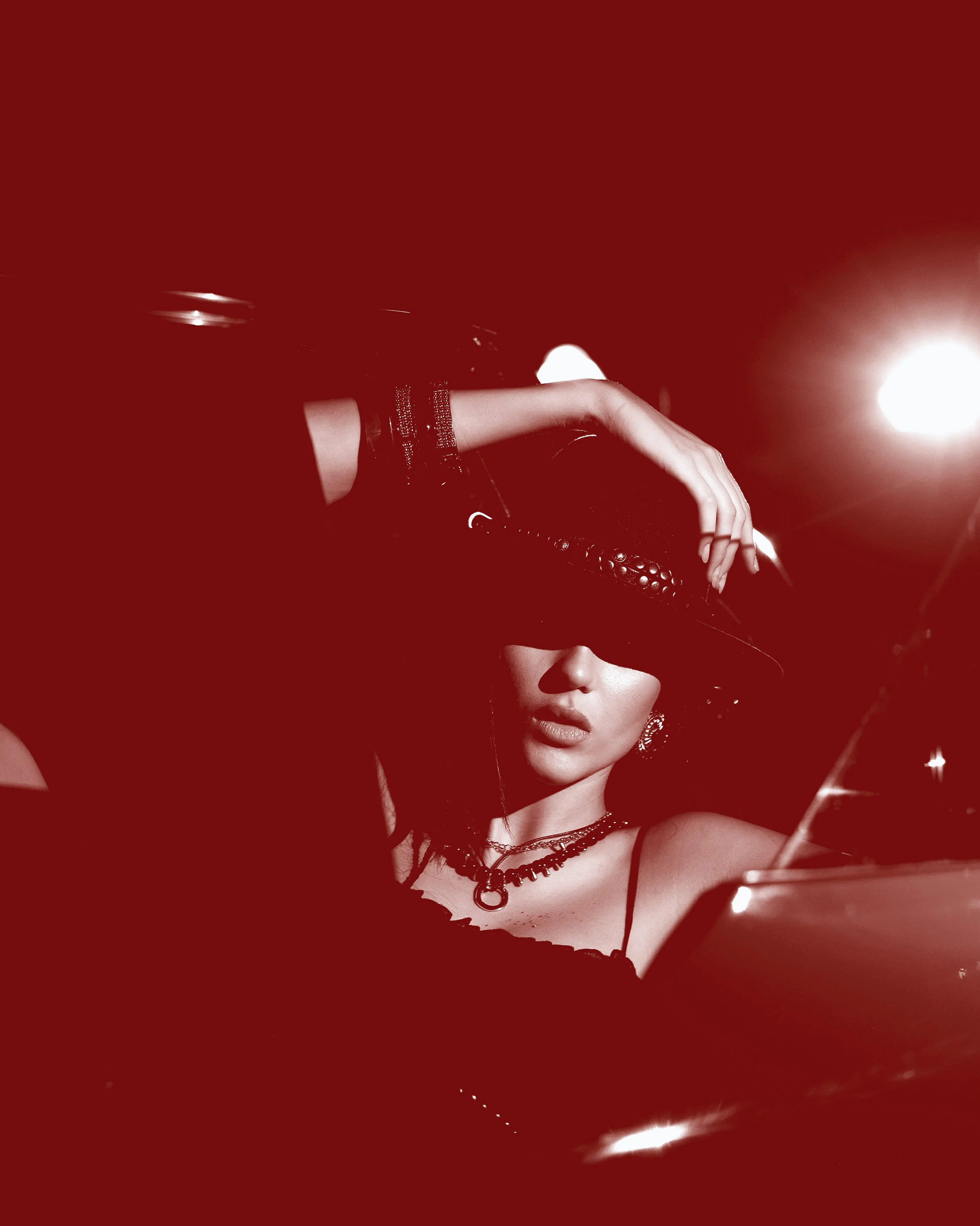 A woman with jewelry, wearing a hat that covers her eyes, posing with a bright light in the background, captured in a fashionable and artistic style.