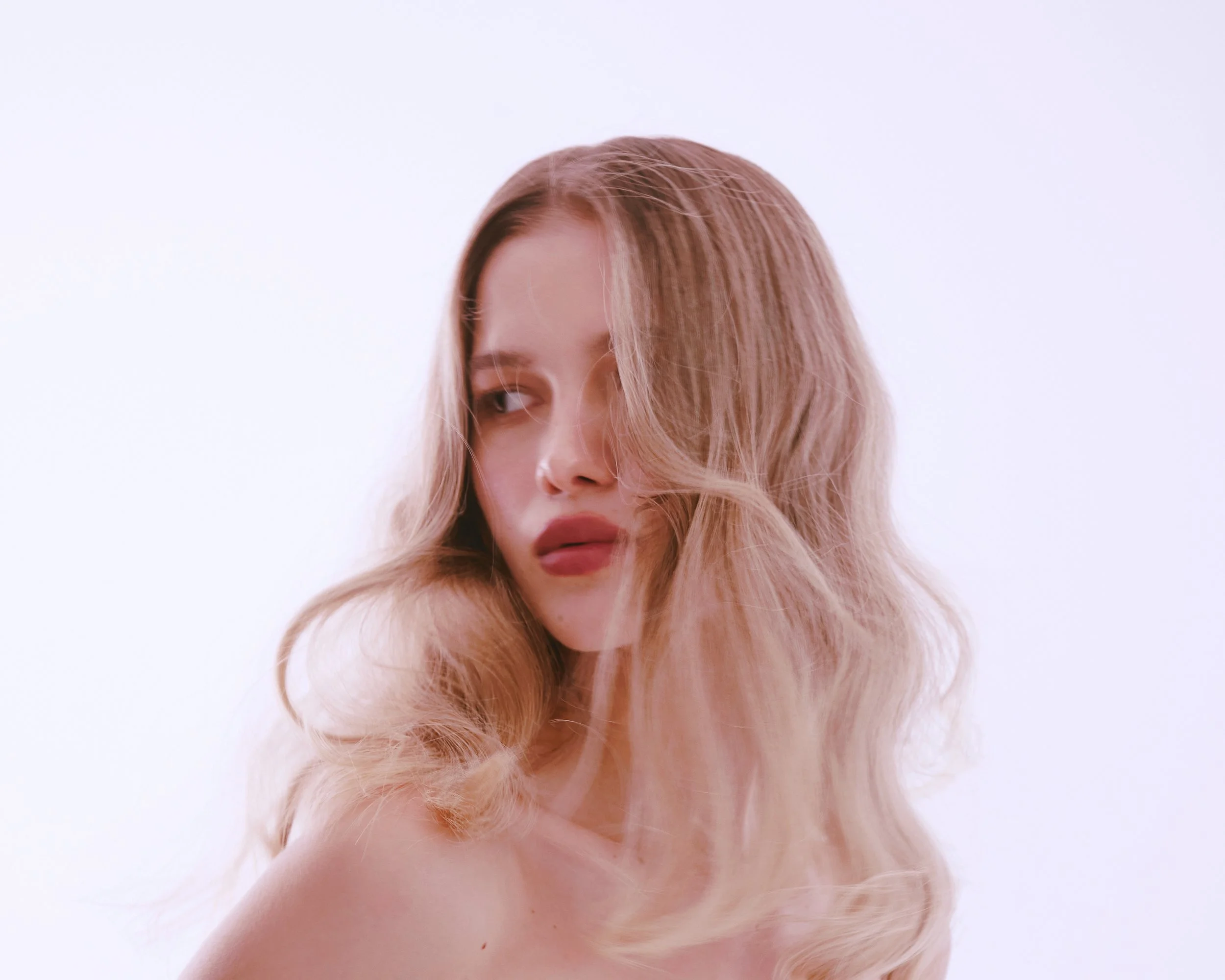 A woman with long, wavy, blonde hair looking to her right with a neutral expression.