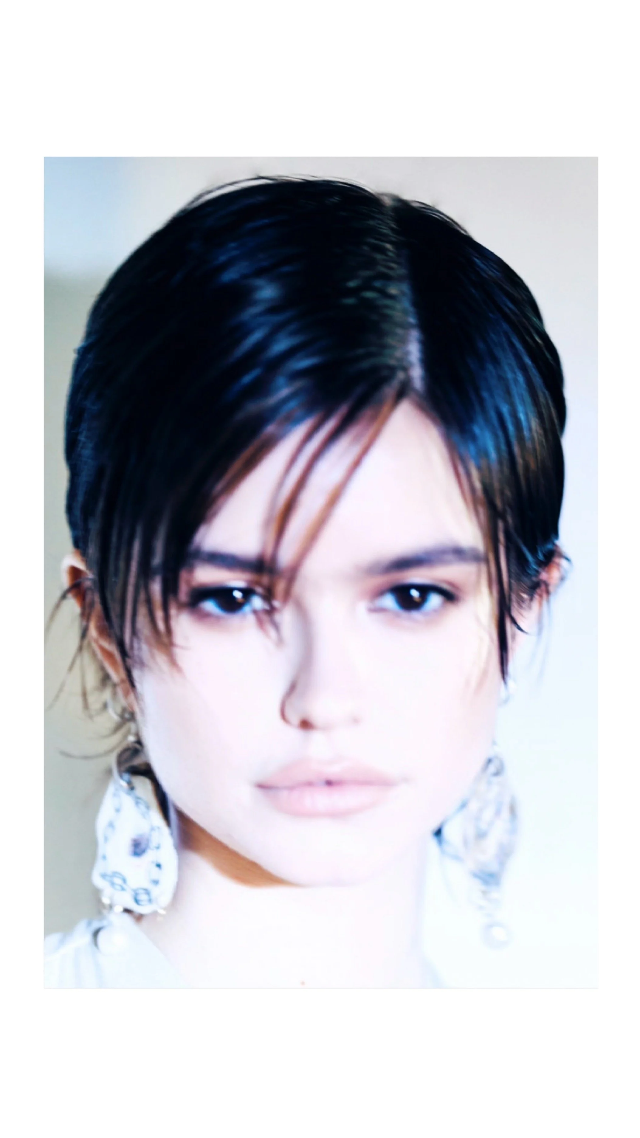 Close-up of a woman with short black hair, light skin, and earrings, looking directly at the camera.