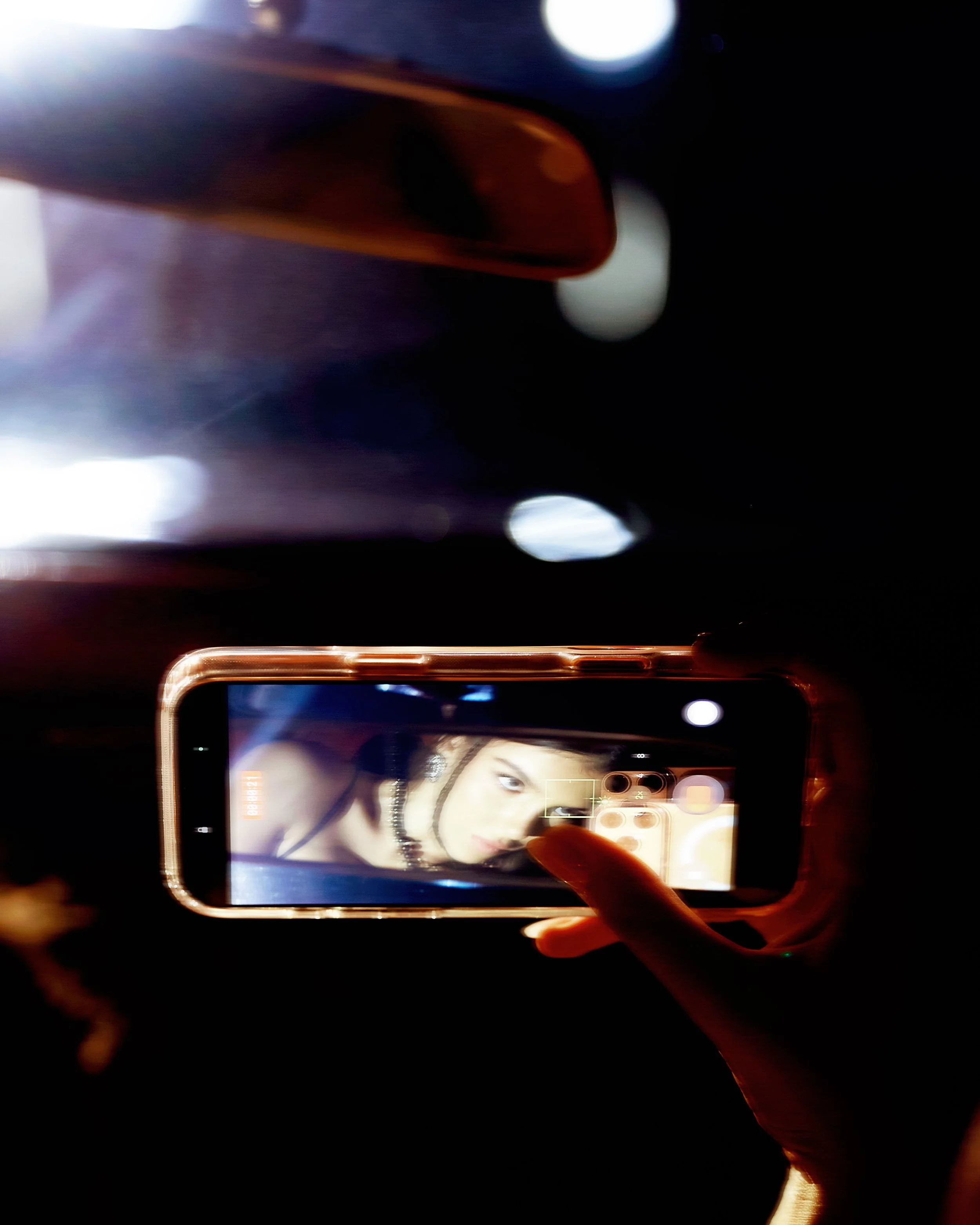 A person holding a smartphone taking a selfie, with the screen displaying their face and shoulder.