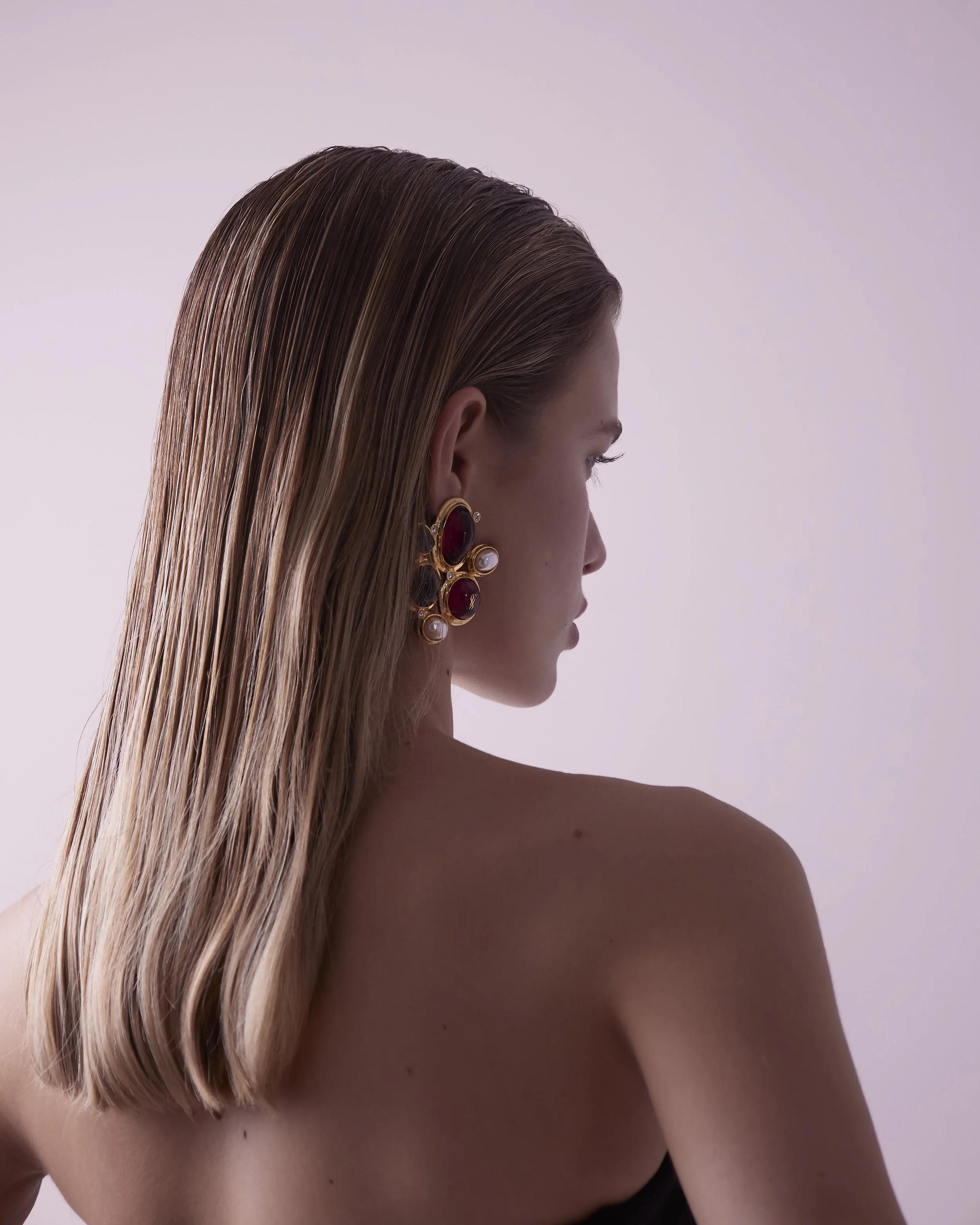 Side profile of a woman with long, straight brown hair wearing an ornate earring with red and pearl elements.