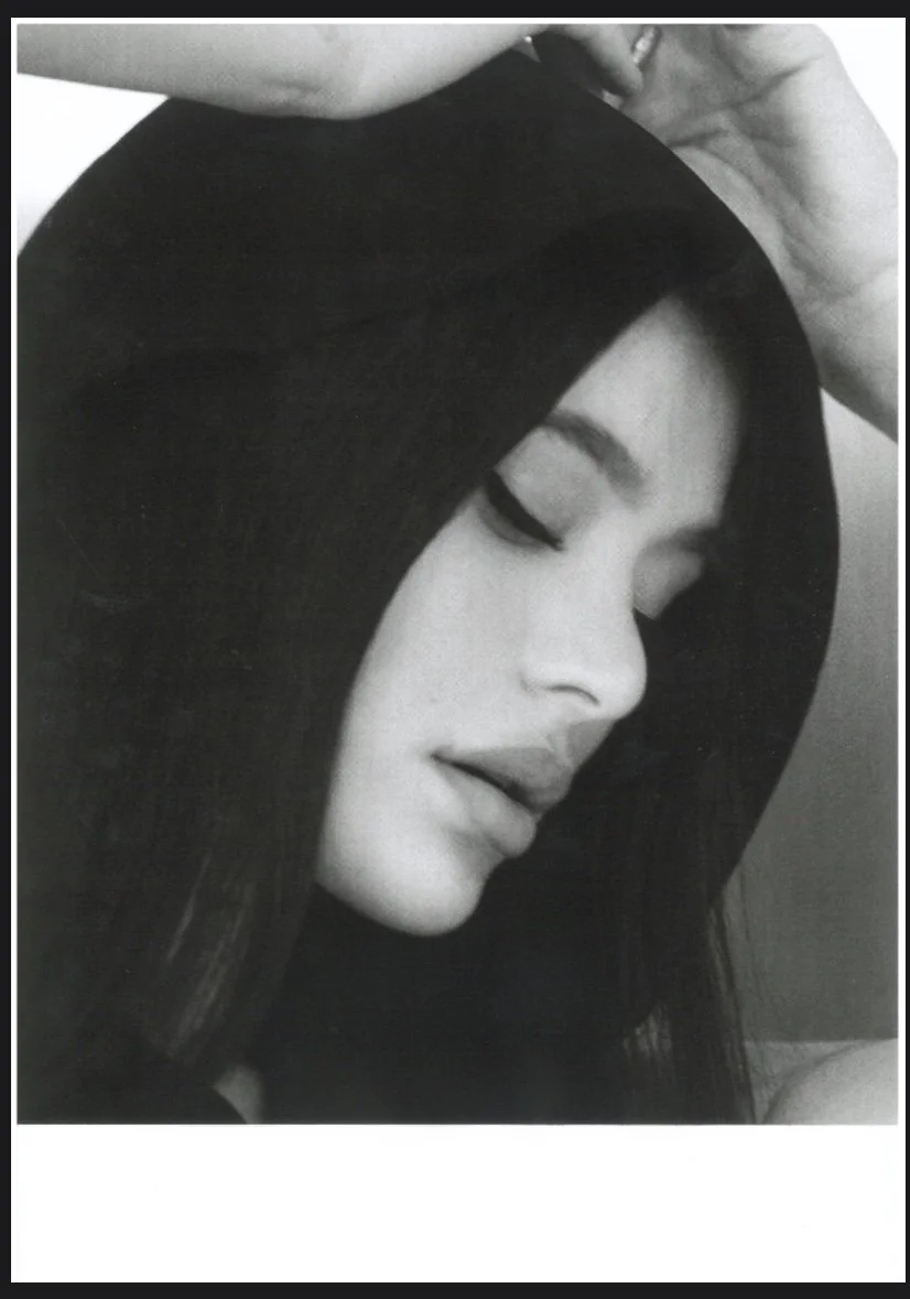 A black and white close-up photograph of a woman with dark, straight hair covering part of her face, her eyes closed, and her lips slightly parted.