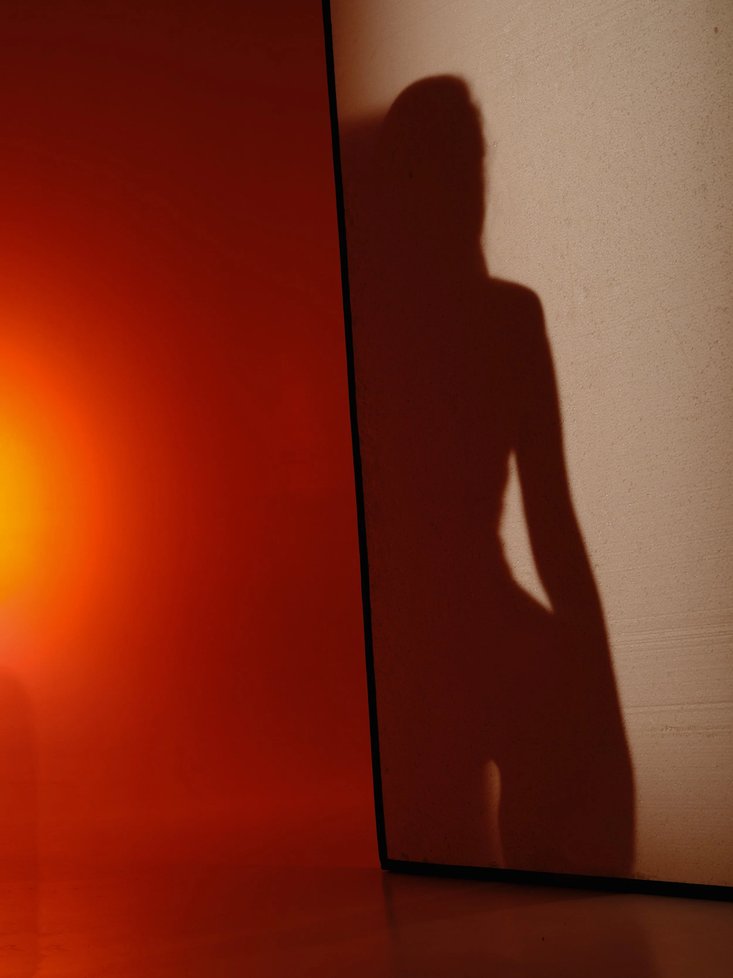 The shadow of a person cast on a wall with a reddish light effect, seen from the side.
