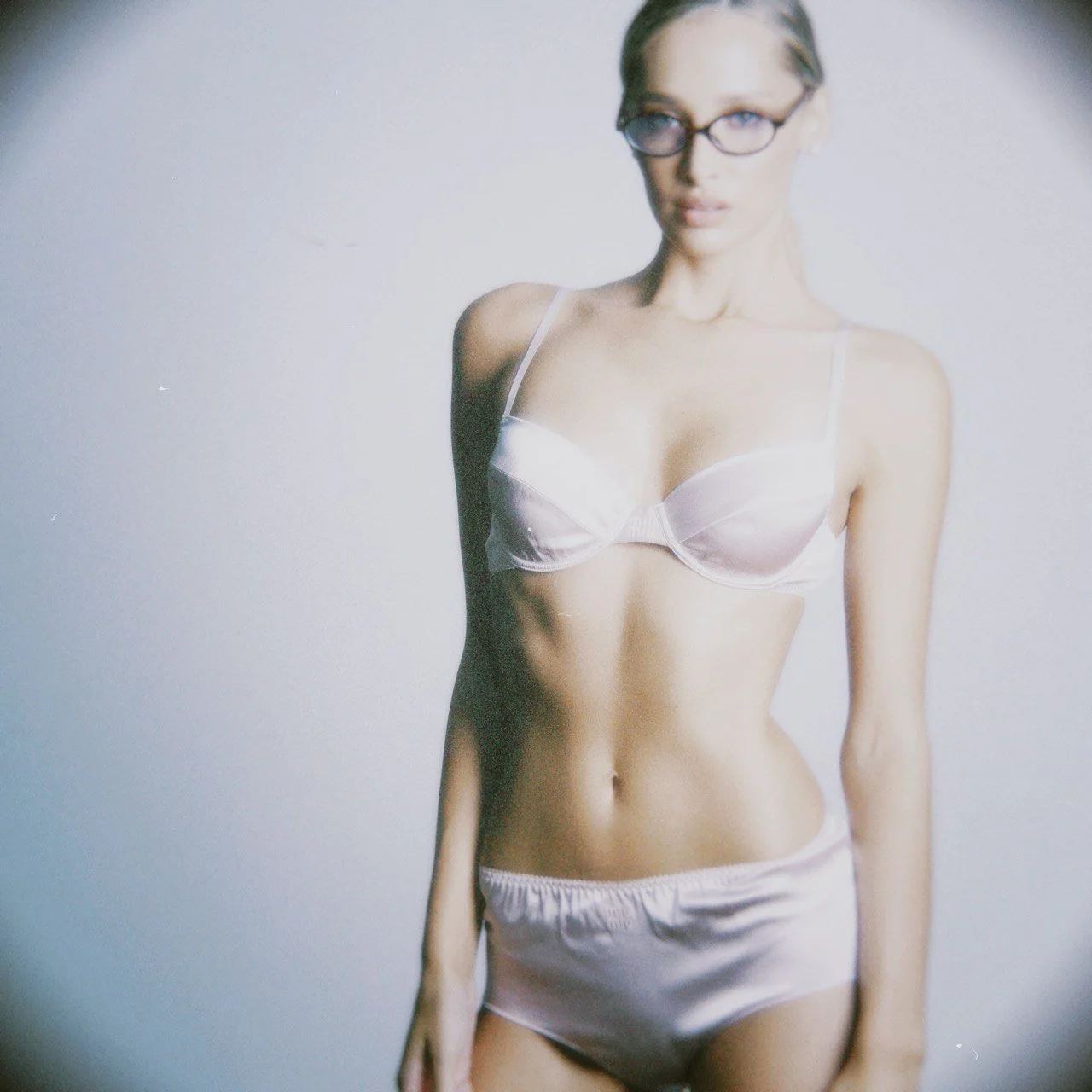 Female model with glasses wearing white lingerie, standing against a light gray background.