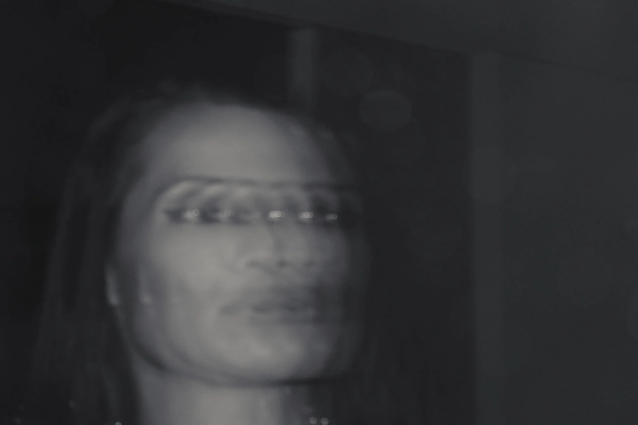 Blurred black and white photo of a woman wearing glasses with a serious expression.