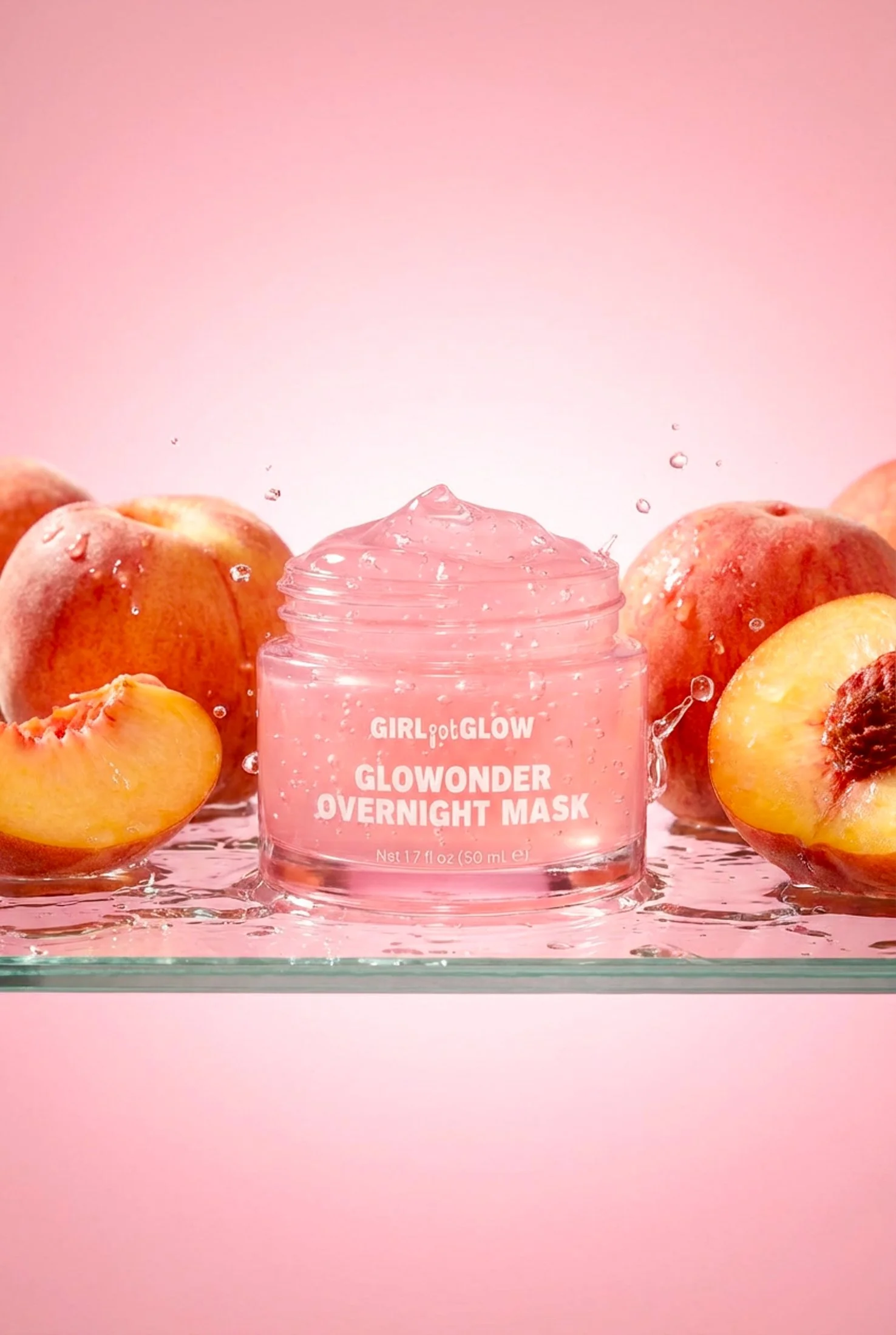 A jar of Girl Got Glow Glow Wonder Overnight Mask surrounded by peaches against a pink background, with some peaches cut open showing the fruit.