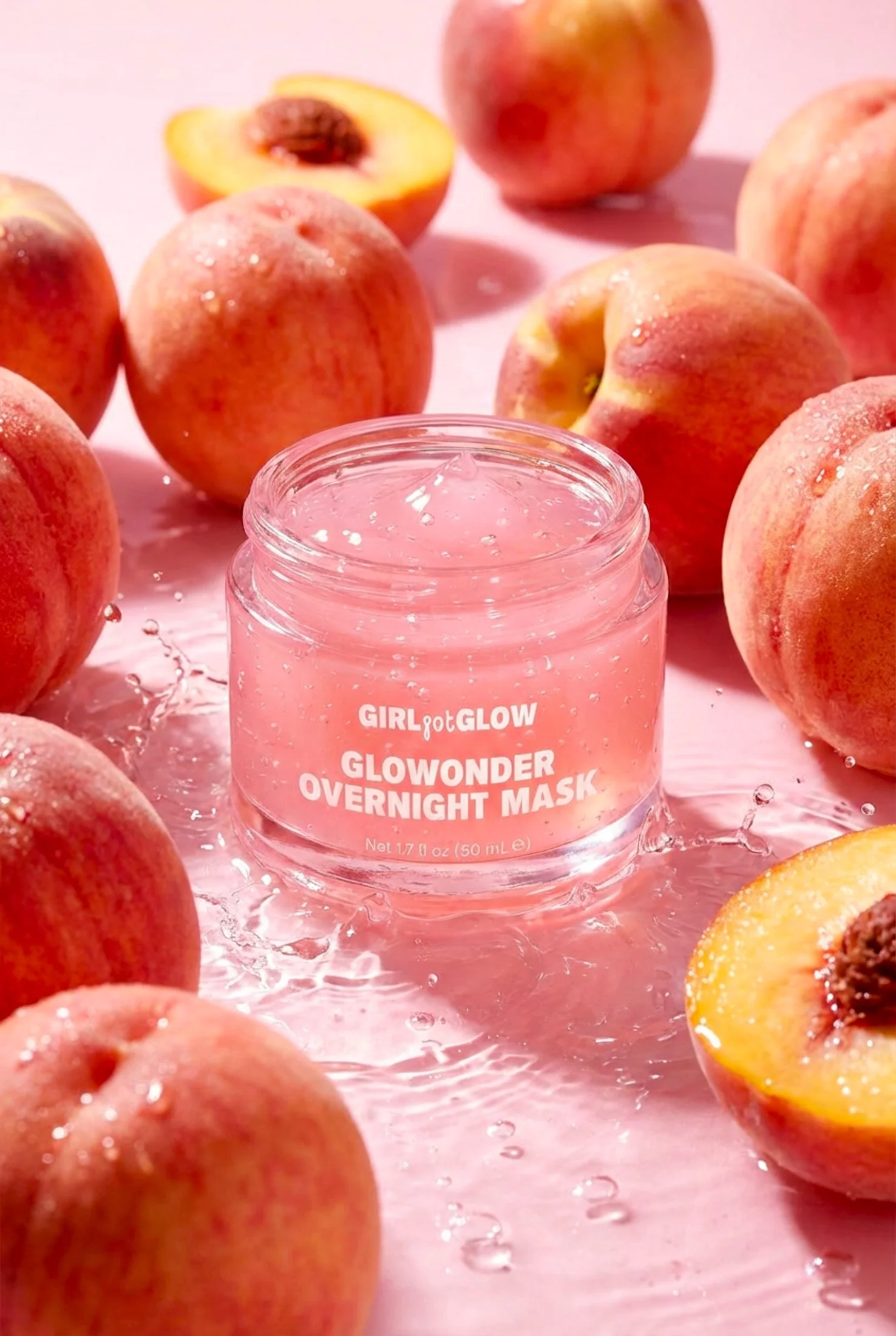 Pink jar of Glowonder Overnight Mask surrounded by whole and halved peaches on a pink background.