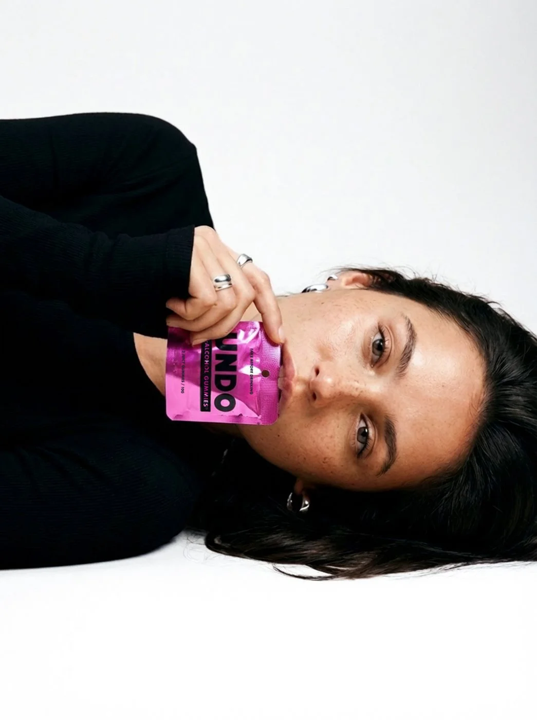 Woman with long dark hair, wearing a black top, holding a pink UNDO pouch.