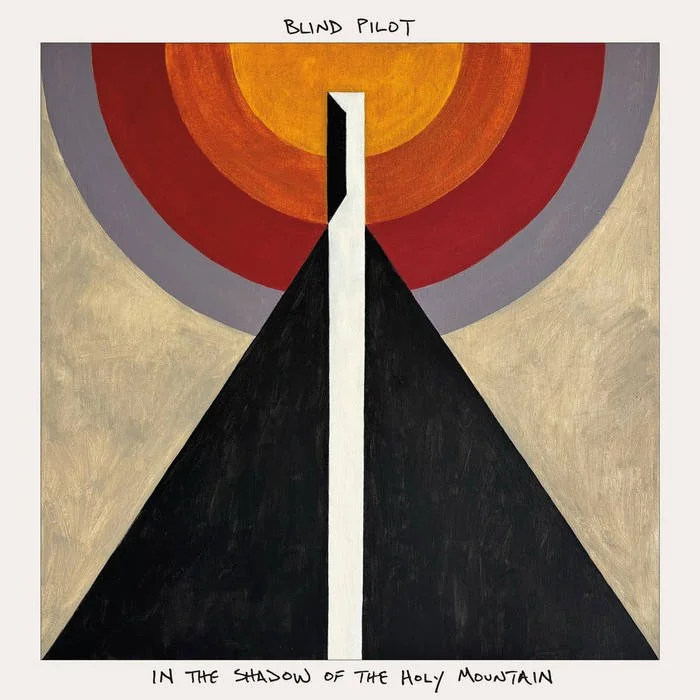 Abstract painting with large black triangle, white vertical line, and concentric circles in red, orange, yellow, gray, and beige at the top and sides. Handwritten text reading 'BLIND PILOT' at top and 'IN THE SHADOW OF THE HOLY MOUNTAIN' at bottom.