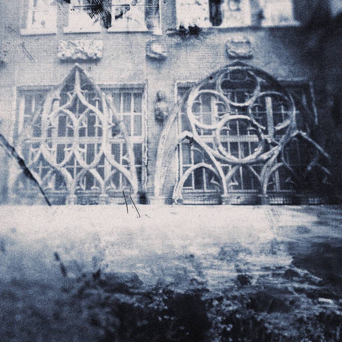 Close-up of an ornate, wrought-iron gate with circular and pointed arch decorative elements, set against a stone building with windows.