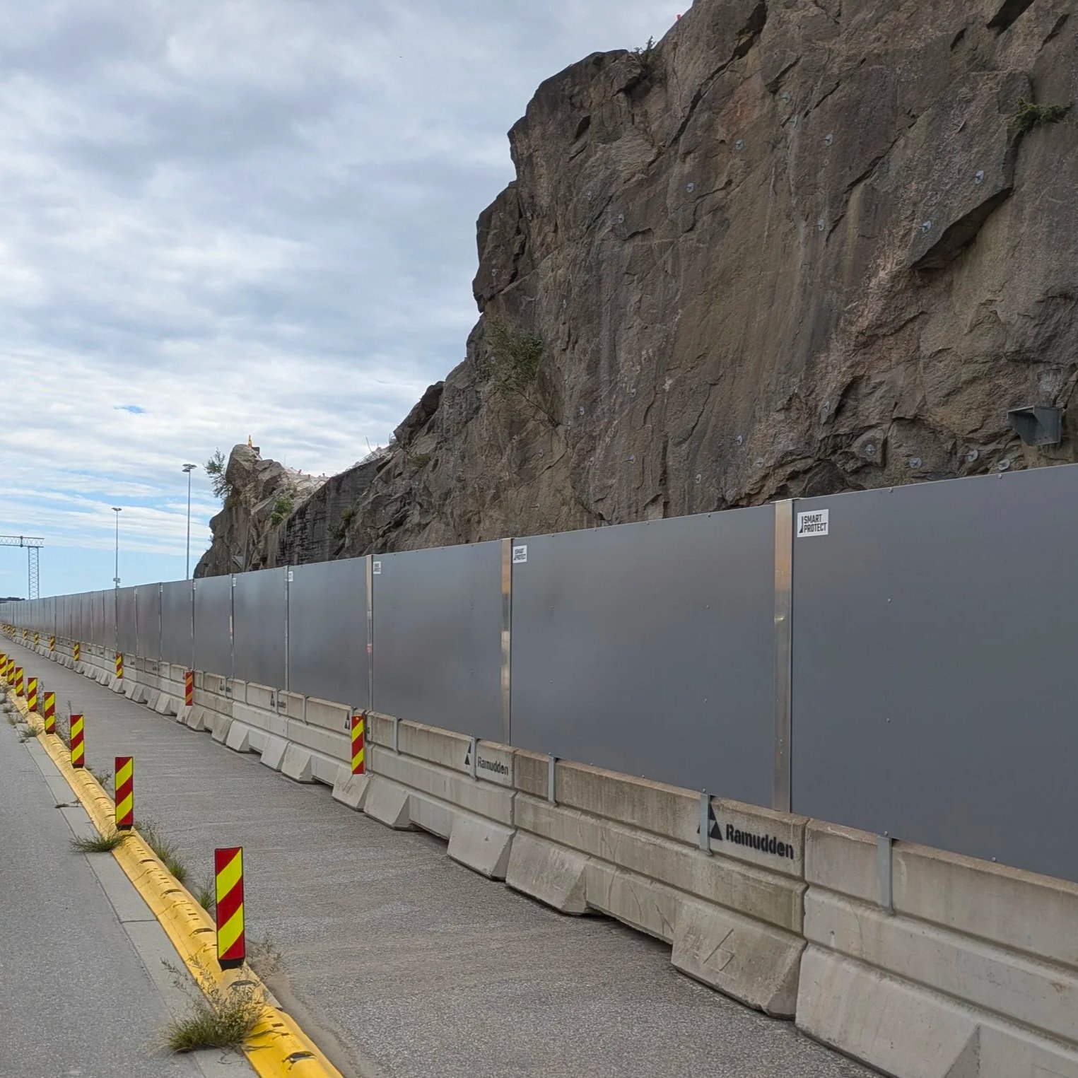 A construction barrier along a road next to a rocky hillside under a cloudy sky.