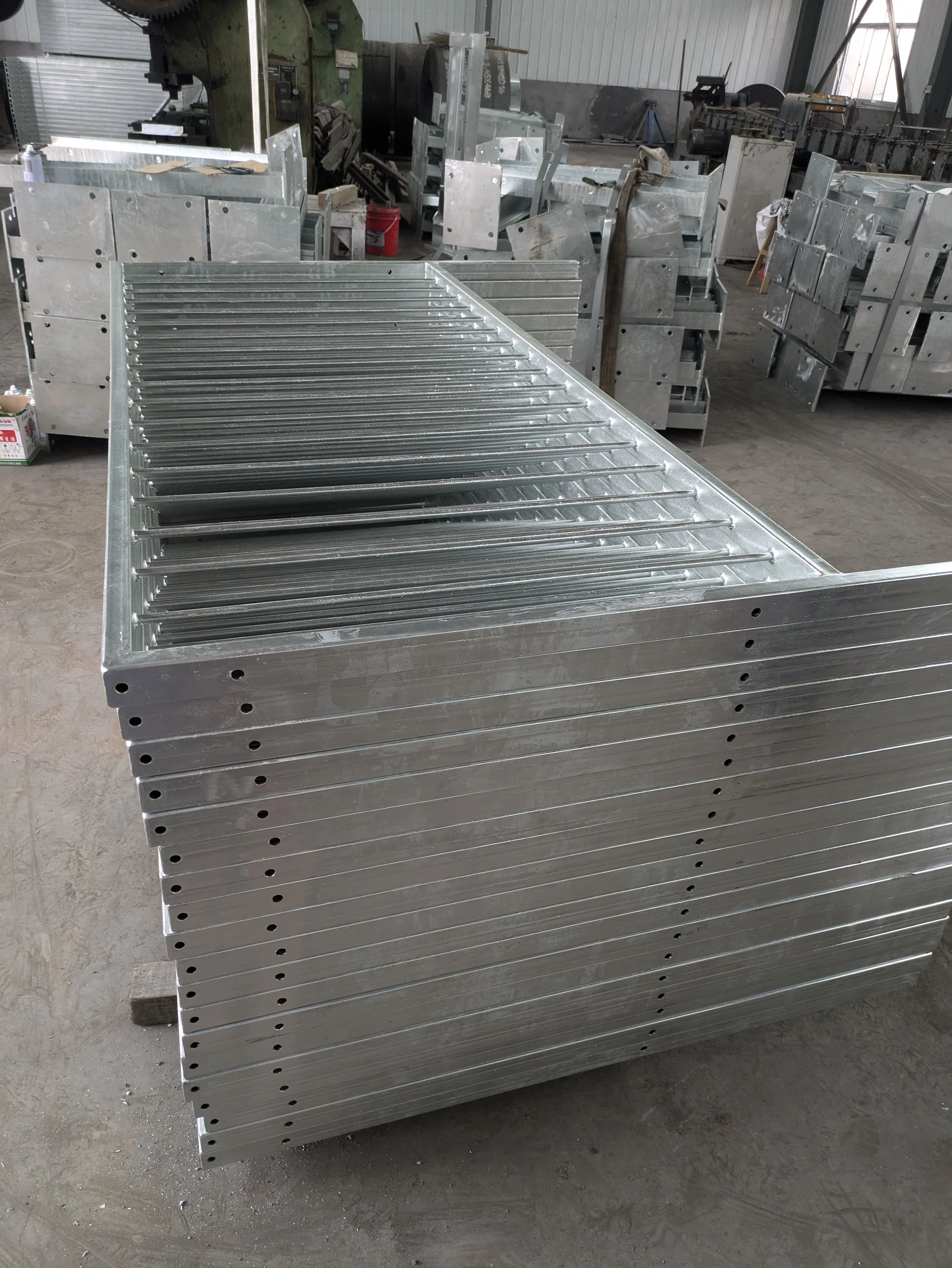 Stack of freshly welded metal components with holes, stored on a pallet in a manufacturing workshop.